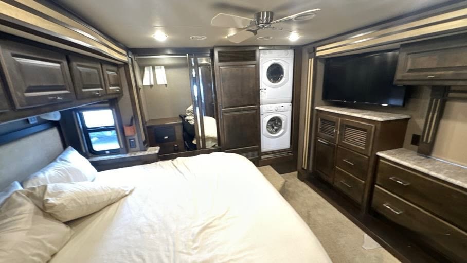 A comfortable RV rental bedroom with a large bed, TV, built-in washer/dryer unit, and ample wooden storage cabinetry.. Tiffin Allegro Red 37PA 2018