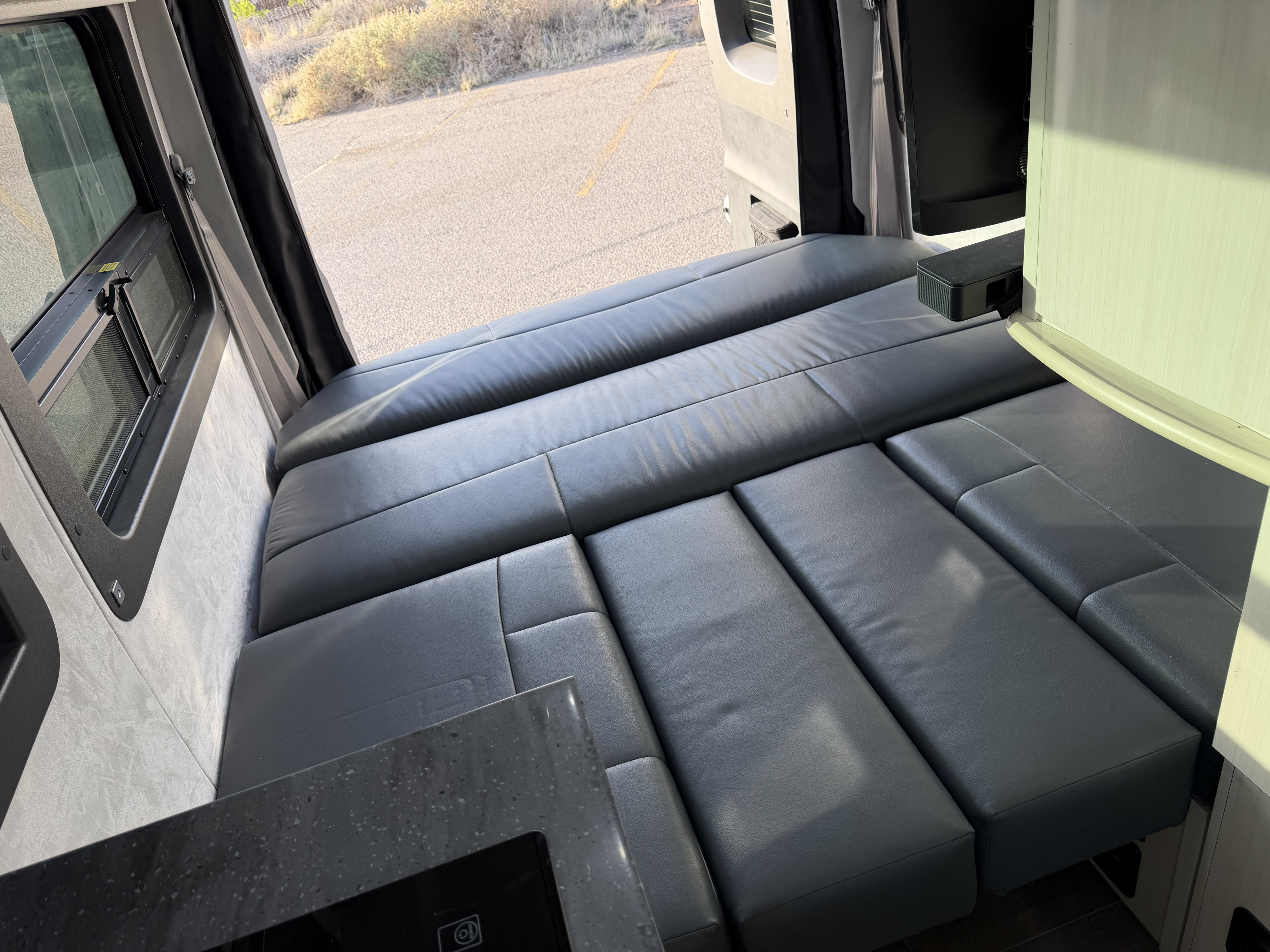Modern rv rental: a versatile gray leatherette bed/seating area, outdoor window view, and integrated kitchen counter visible.. Pleasure-Way Pleasure-Way Class B 2022