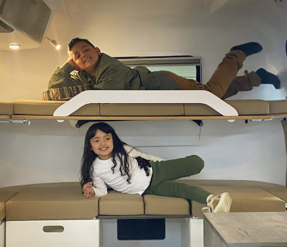 Two smiling kids relaxing in comfy bunk beds inside an RV rental. Ideal for family road trips!. Happier Camper HC1 2022