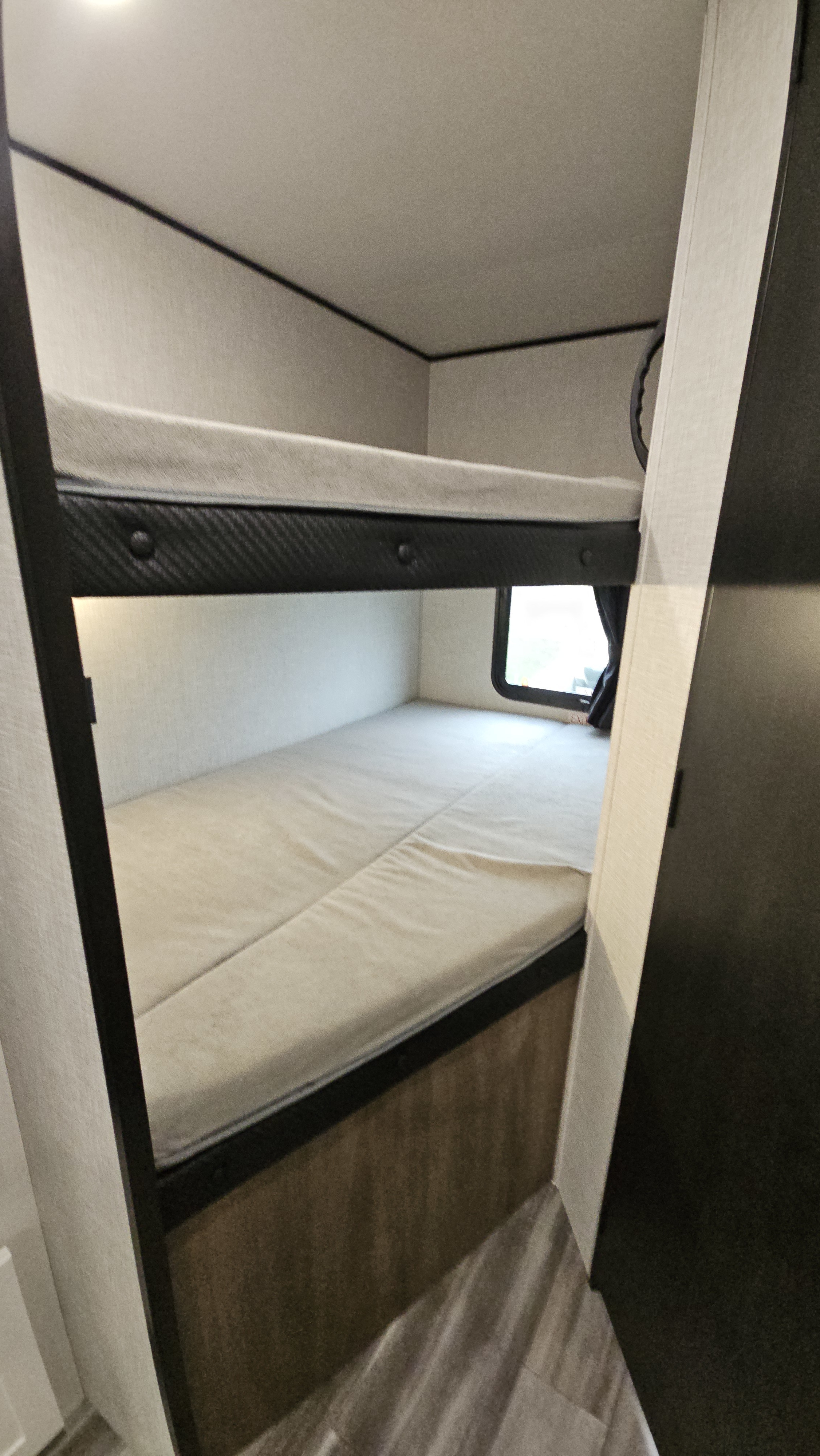 RV rental bunk beds: a cozy, compact camper interior with two light-colored mattresses, a window, and dark trim.. Jayco Jay Flight SLX 2025