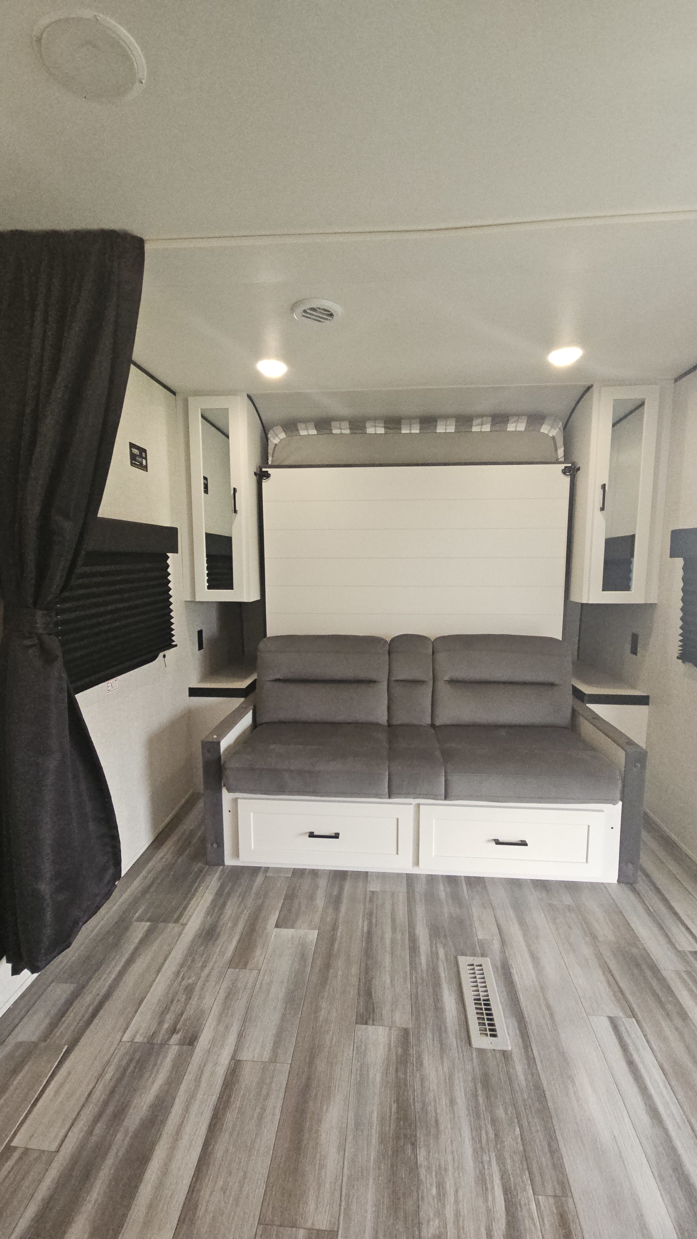This RV rental interior features a gray sofa with storage drawers, a folded-up murphy bed, and compact cabinets.. Jayco Jay Flight SLX 2025
