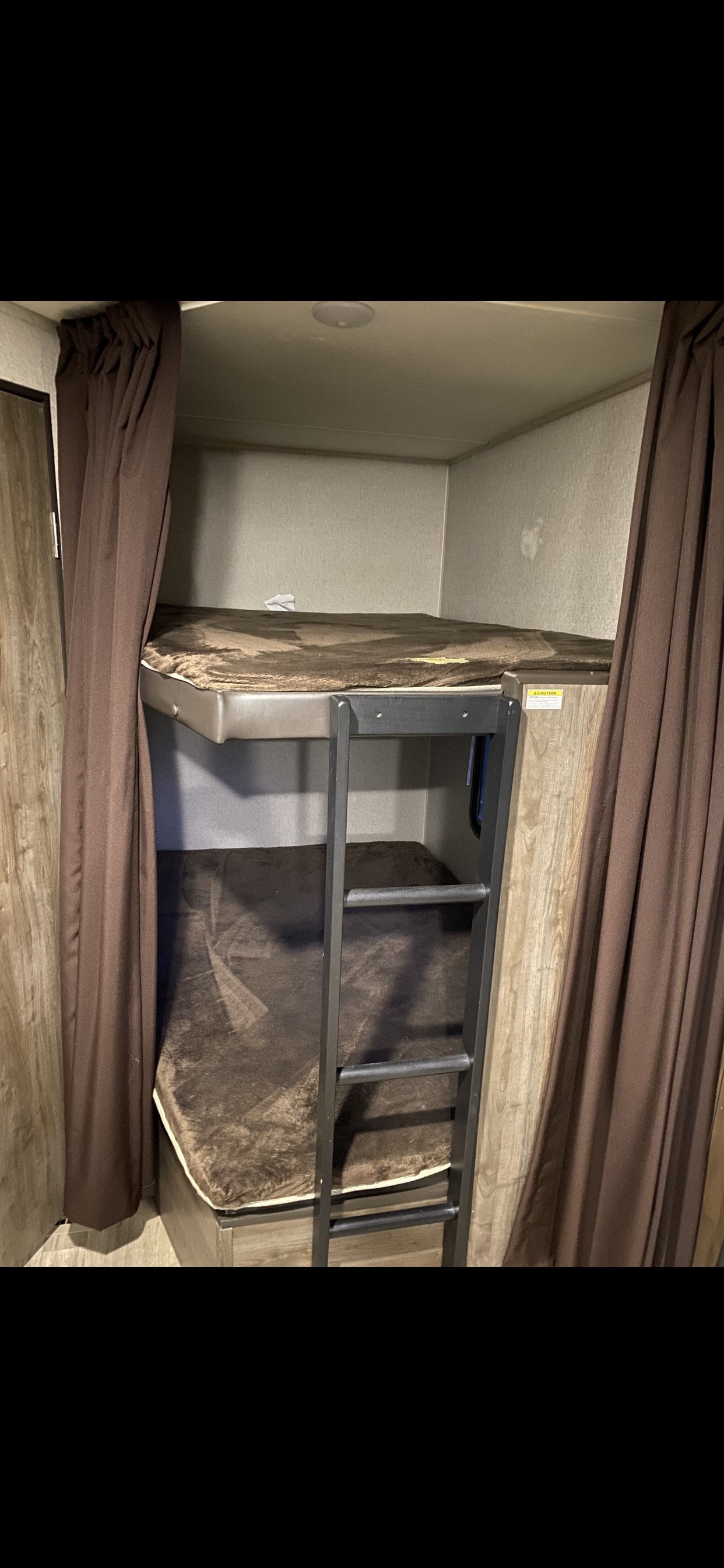 Cozy bunk beds in an rv rental, complete with a ladder and warm brown curtains and bedding.. Dutchmen Coleman Lantern 2018