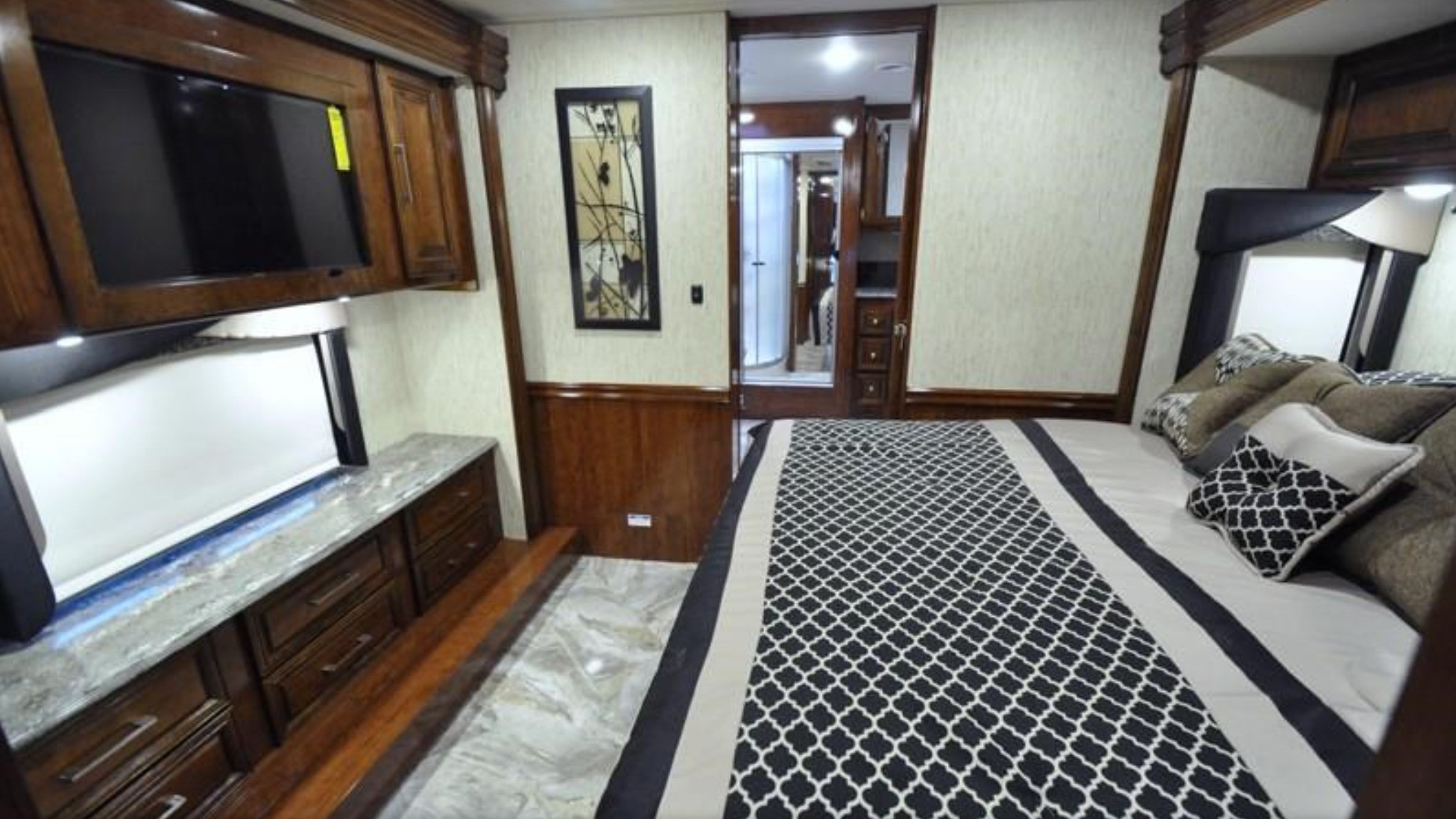 Luxurious RV rental bedroom features a large bed with patterned bedding, wall-mounted TV, and elegant wood cabinetry.. Coachmen Sportscoach 2018