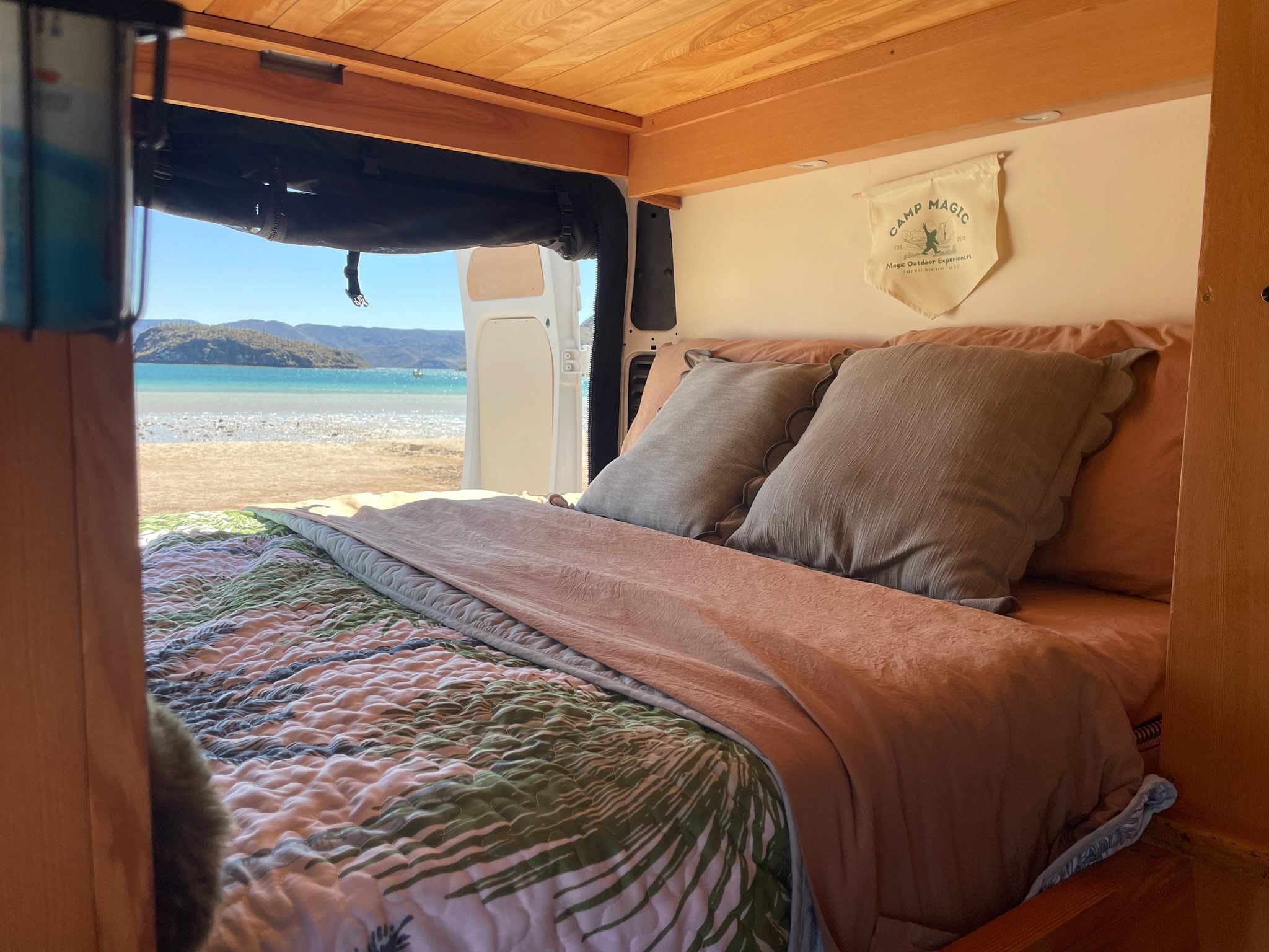Inside a cozy rv rental, a made bed with a quilt opens to a stunning beach and ocean view.. Dodge 1500 2018