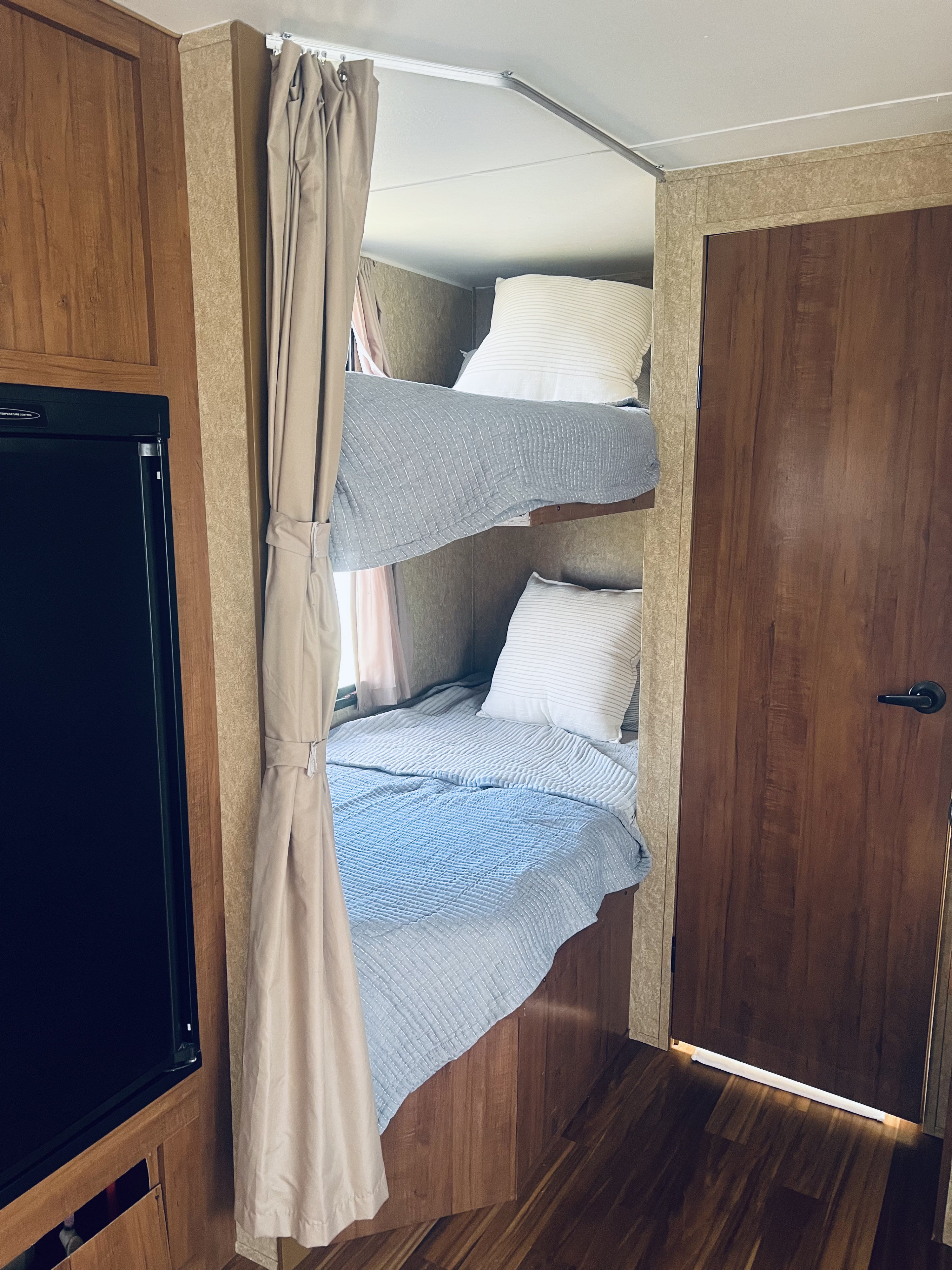 An RV rental's cozy bunk beds, featuring light blue and white bedding, pillows, and privacy curtains for a comfortable camper interior.. Gulf Stream Kingsport 2013