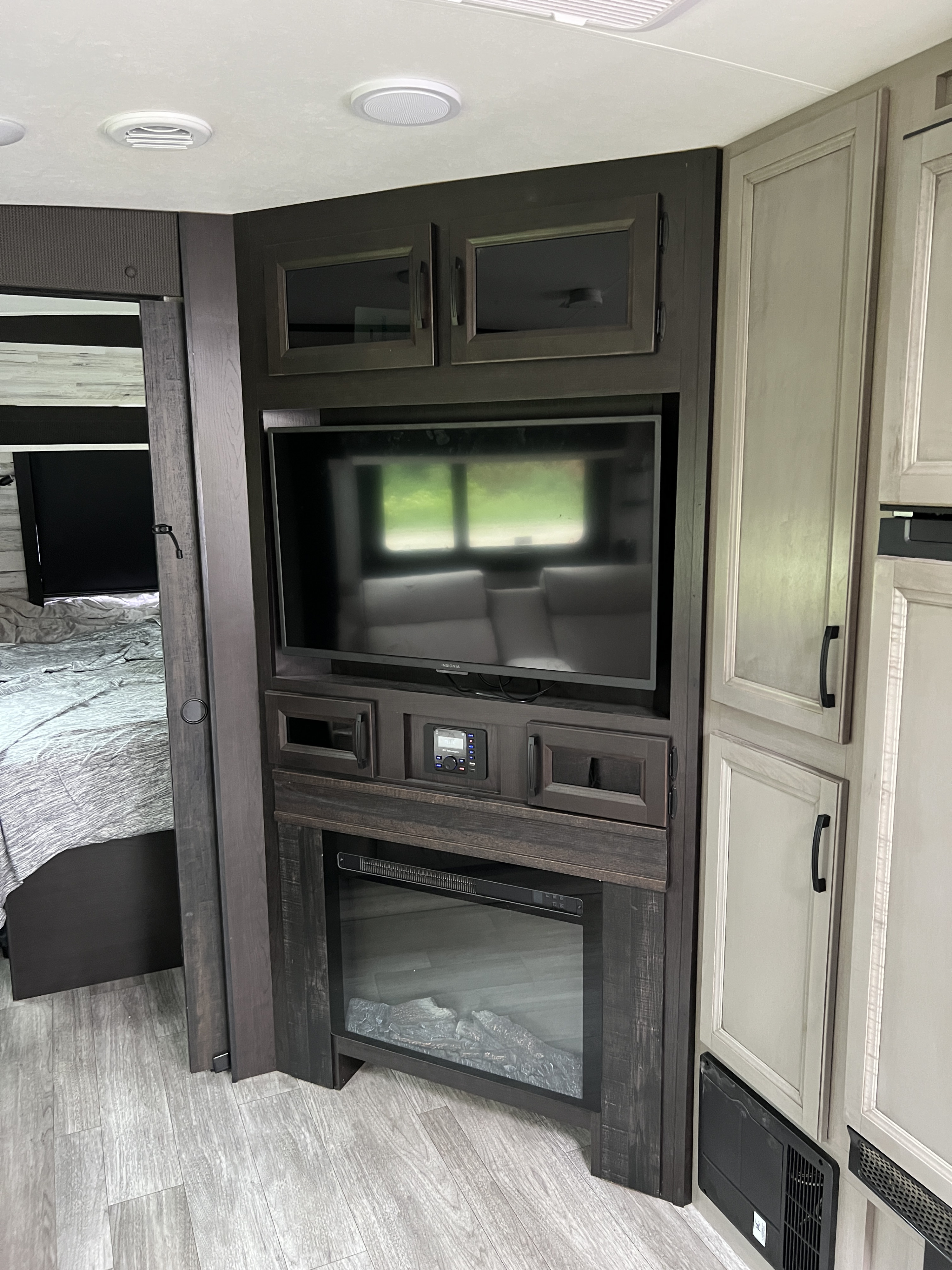 RV rental interior: A media console with TV, electric fireplace, dark wood cabinets, and light flooring. A bedroom entrance is visible.. Jayco White Hawk 2022