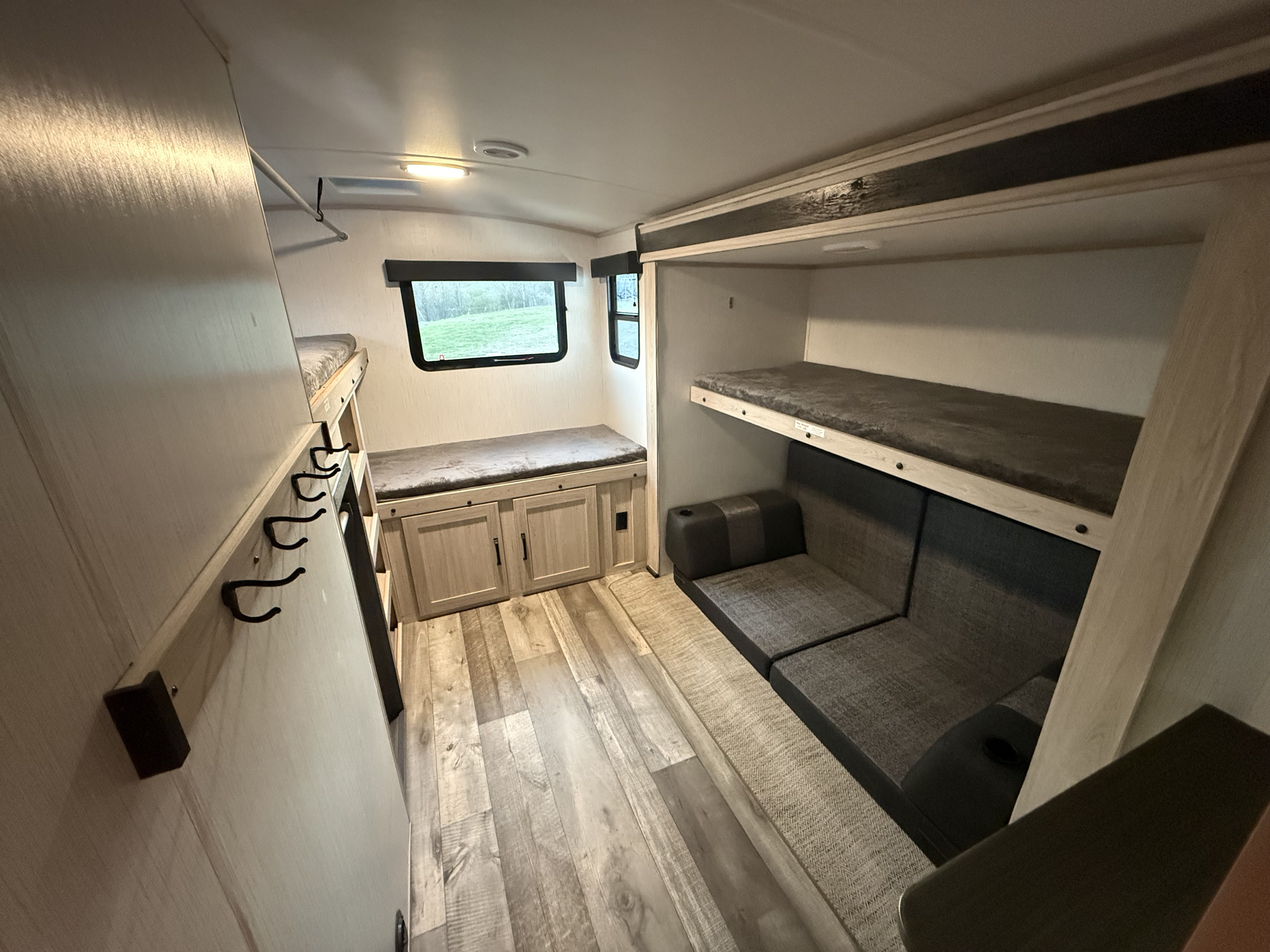 RV rental bunk room: Interior with bunk beds, sofa, bench storage, windows. Features wood-look floor, overhead light, and coat hooks.. Heartland RVs Sundance Ultra Lite 2022