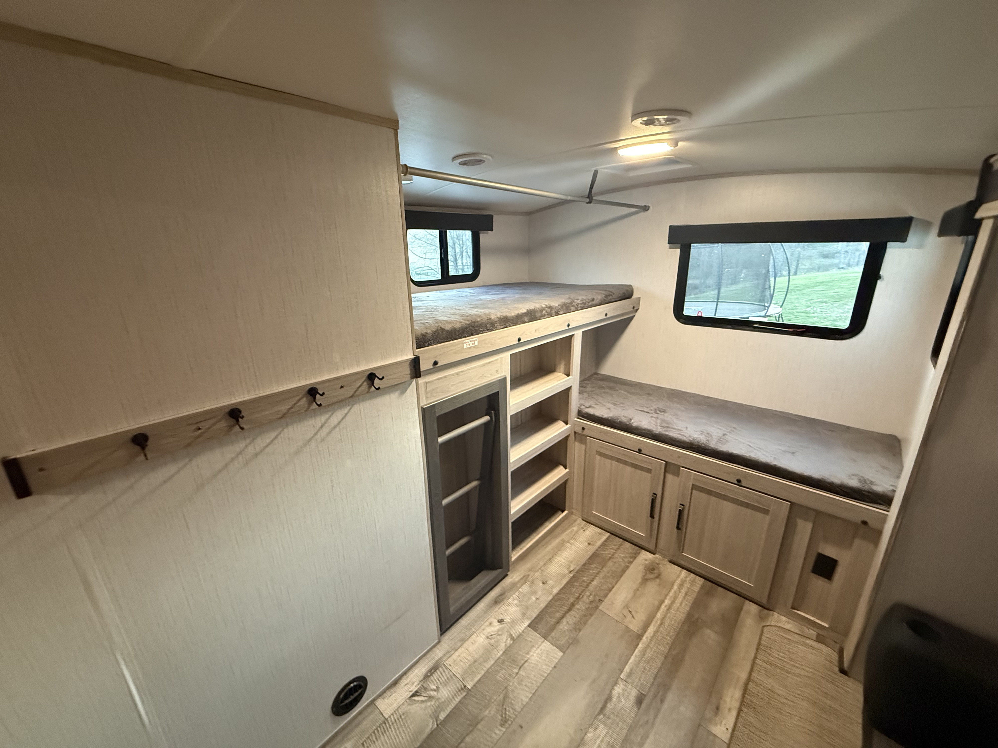 RV rental bunk beds with plush mattresses, integrated storage shelves, a hanging rod, and wall hooks for organized travel.. Heartland RVs Sundance Ultra Lite 2022