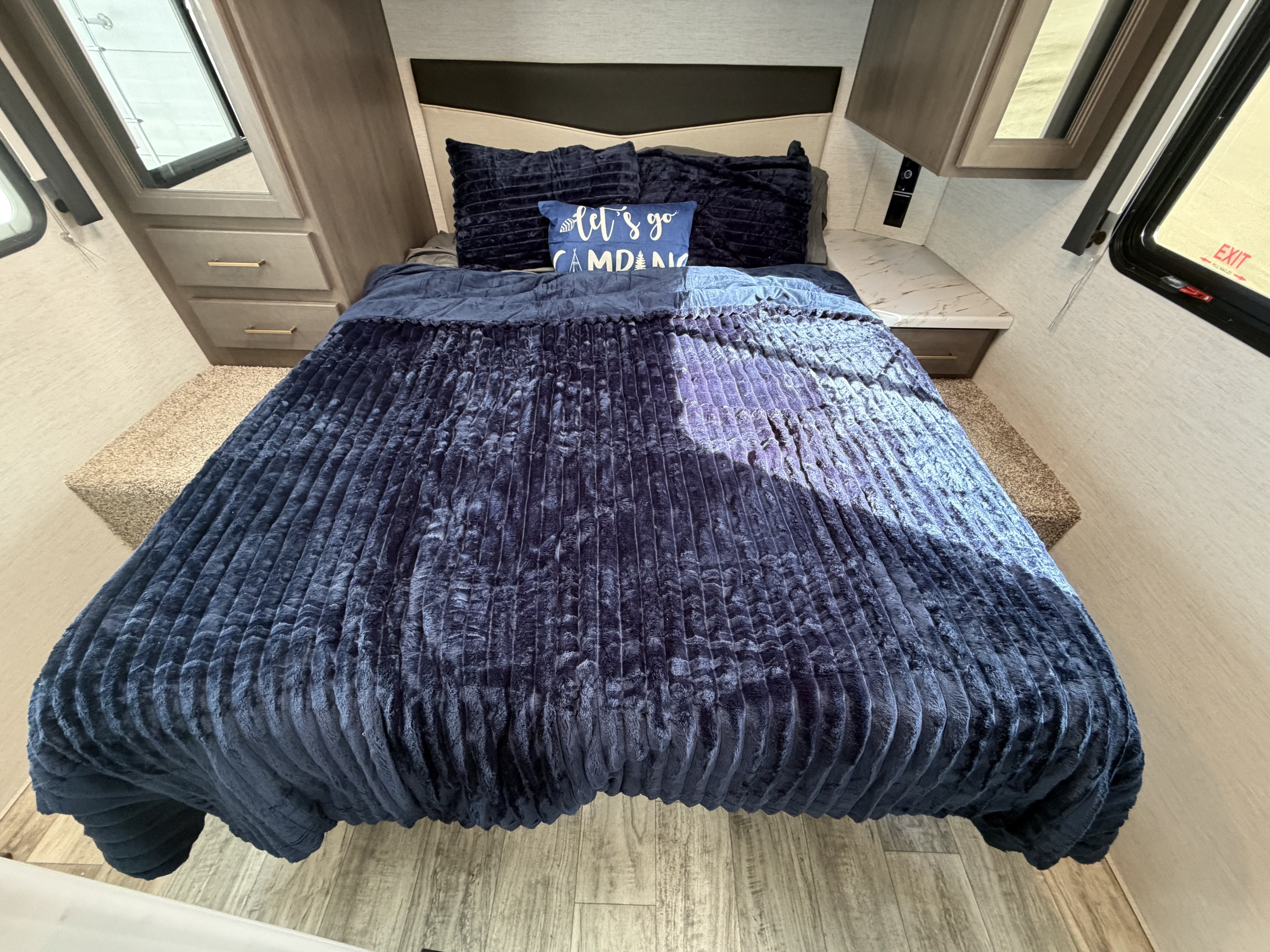 Cozy RV rental bedroom featuring a plush navy blue bed, "Let's Go Camping" pillow, and convenient storage.. Thor Freedom Elite 2023