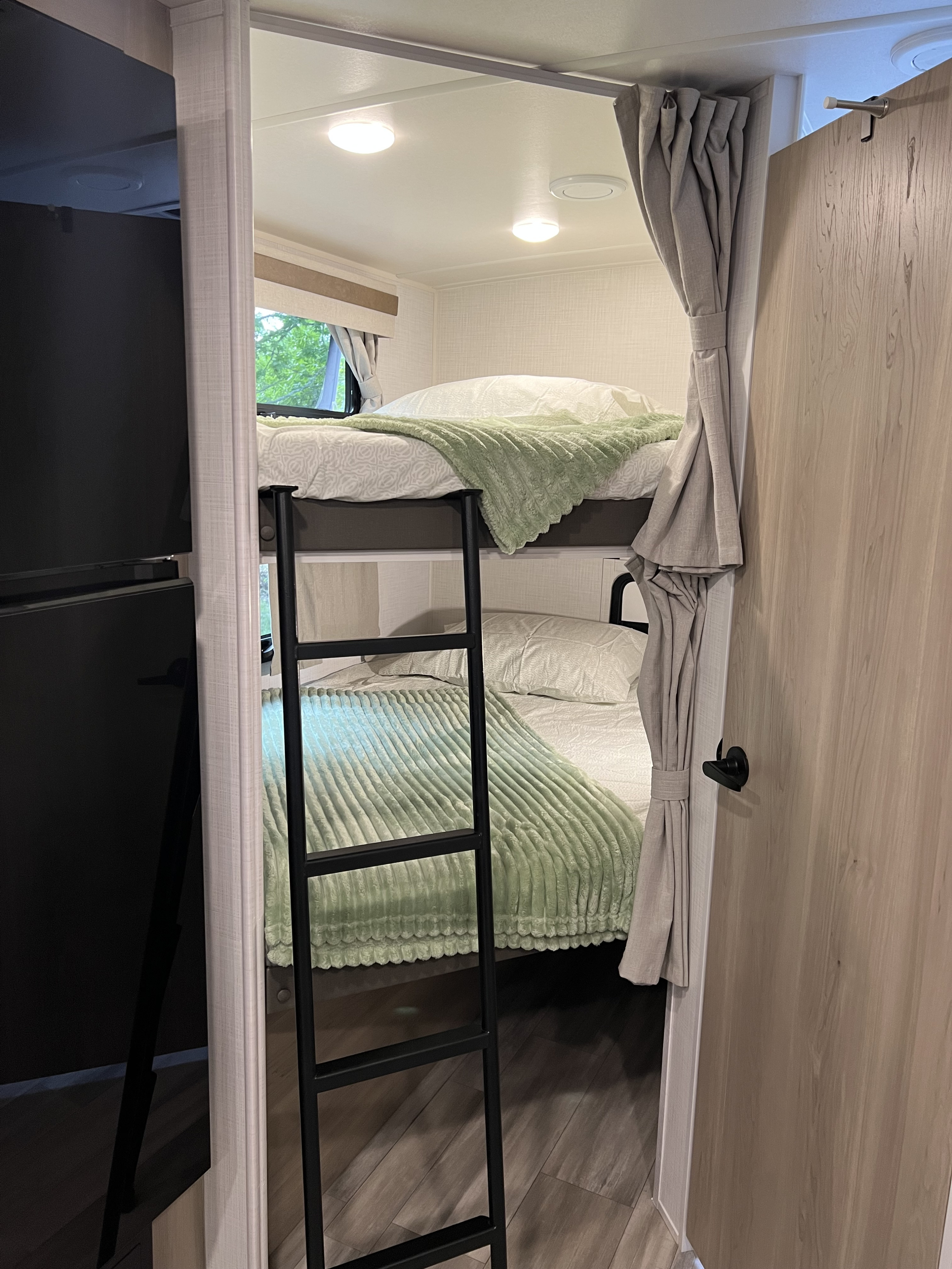 Cozy RV rental interior with bunk beds, a black ladder, soft green & white bedding, & window view. Perfect camper sleeping area.. Forest River Rockwood Mini Lite 2024