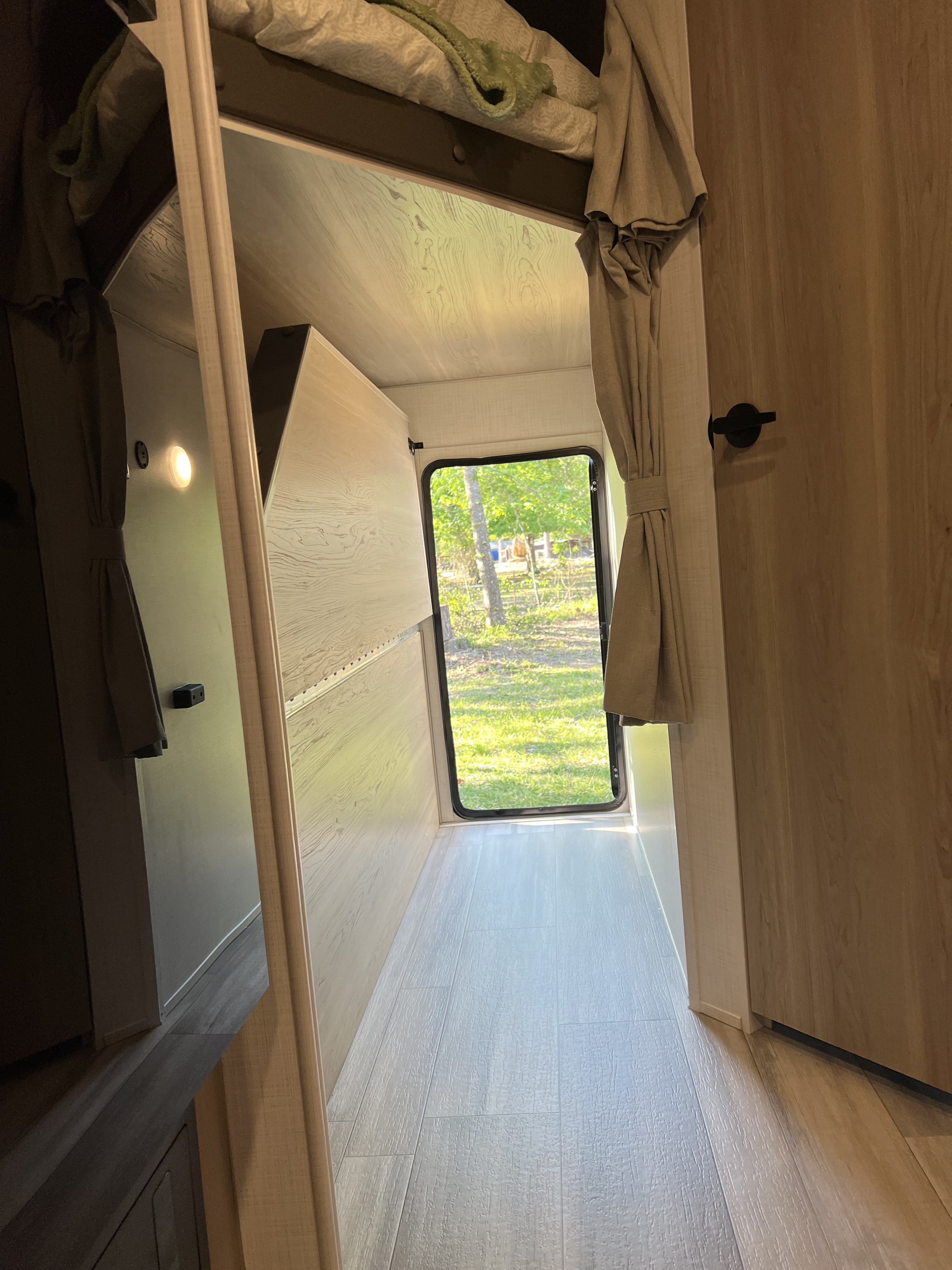 Bright RV rental interior hallway with bunk bed, mirror, and outdoor view through the back window.. Forest River Rockwood Mini Lite 2024