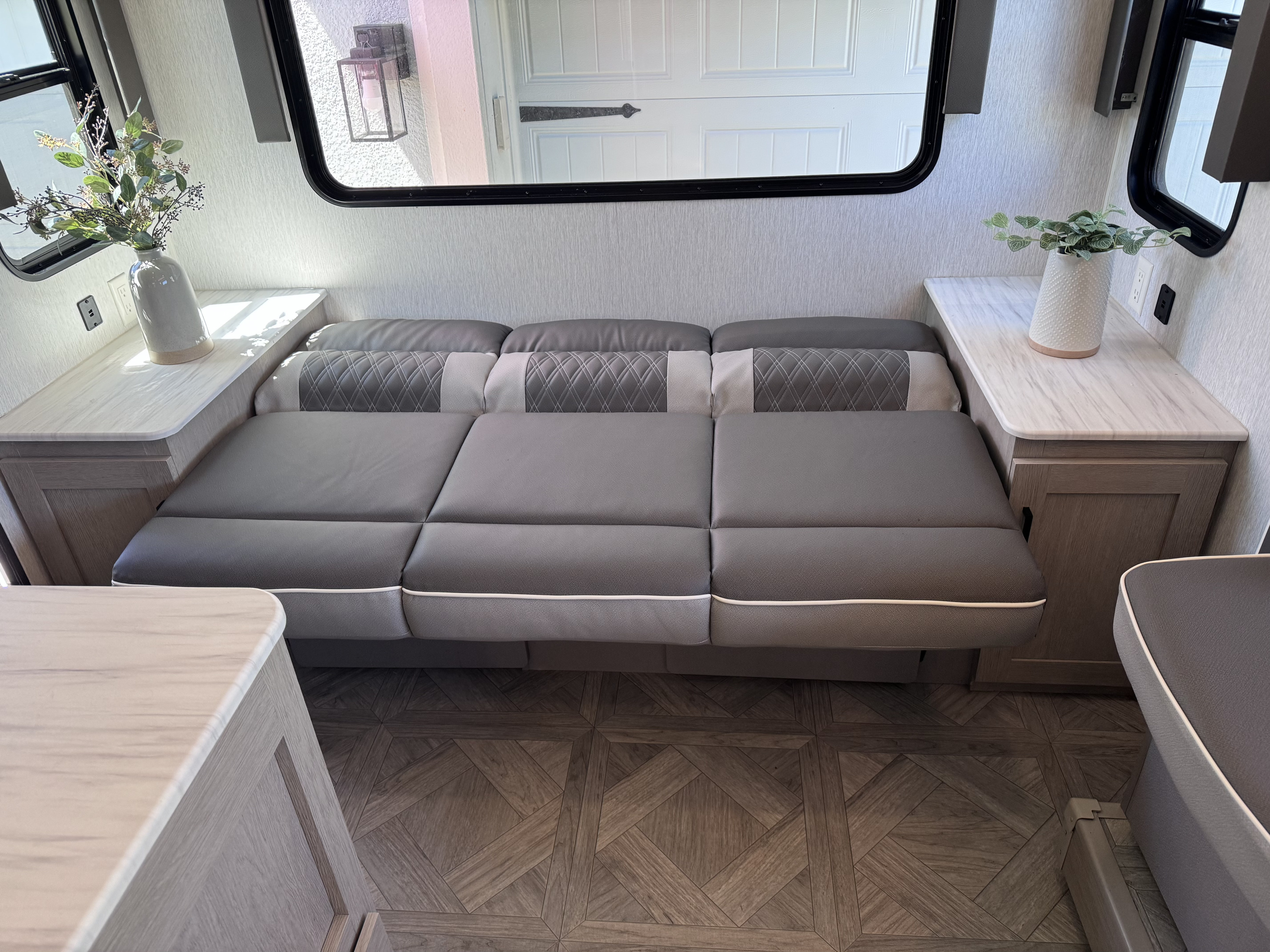 RV rental interior features a gray sofa-bed, patterned wood floor, and side tables by windows, offering comfort.. Forest River Salem Cruise Lite Platinum 2023