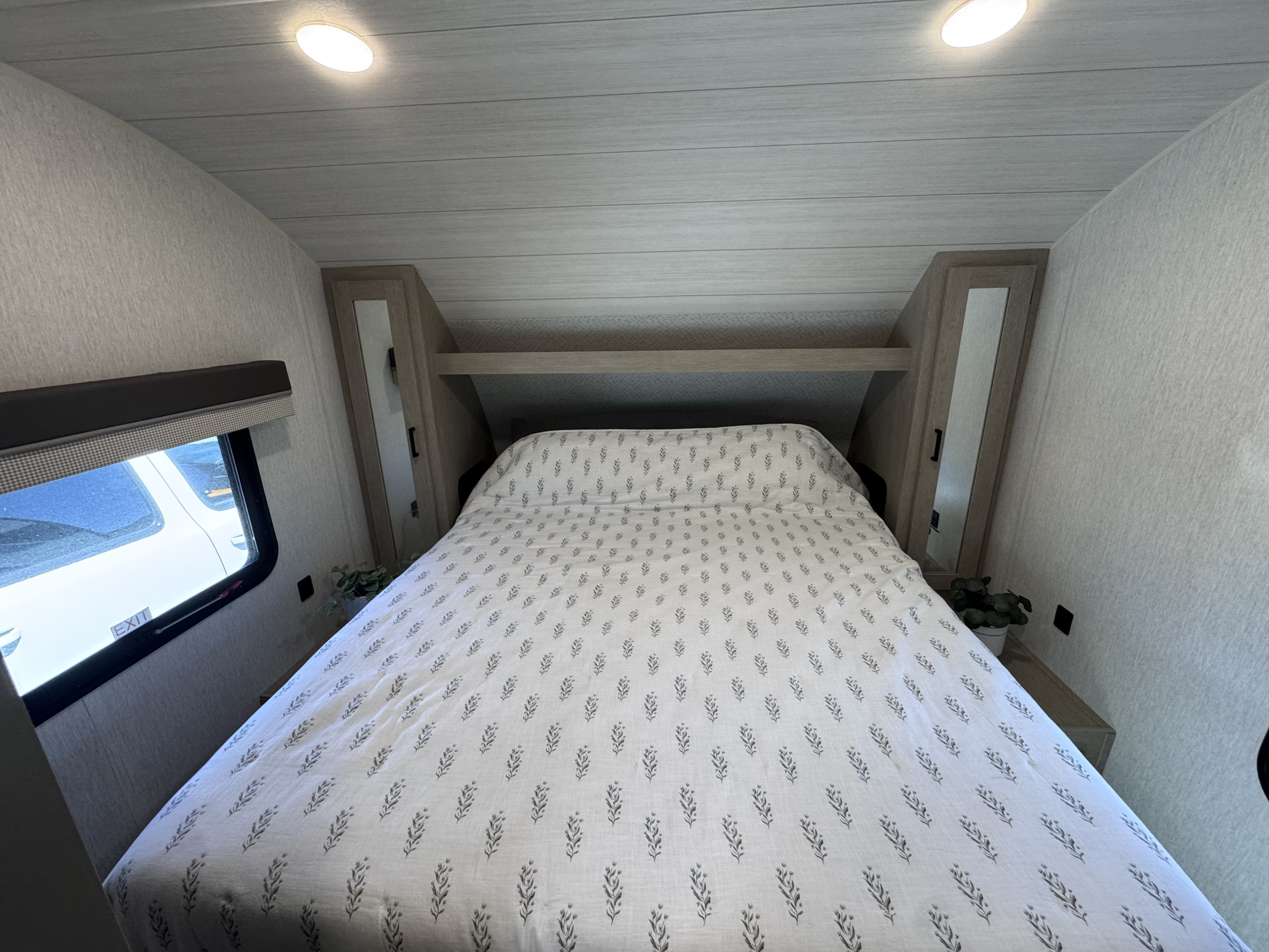RV rental bedroom interior, featuring a bed with leaf-patterned bedding, overhead storage, and a window.. Forest River Salem Cruise Lite Platinum 2023