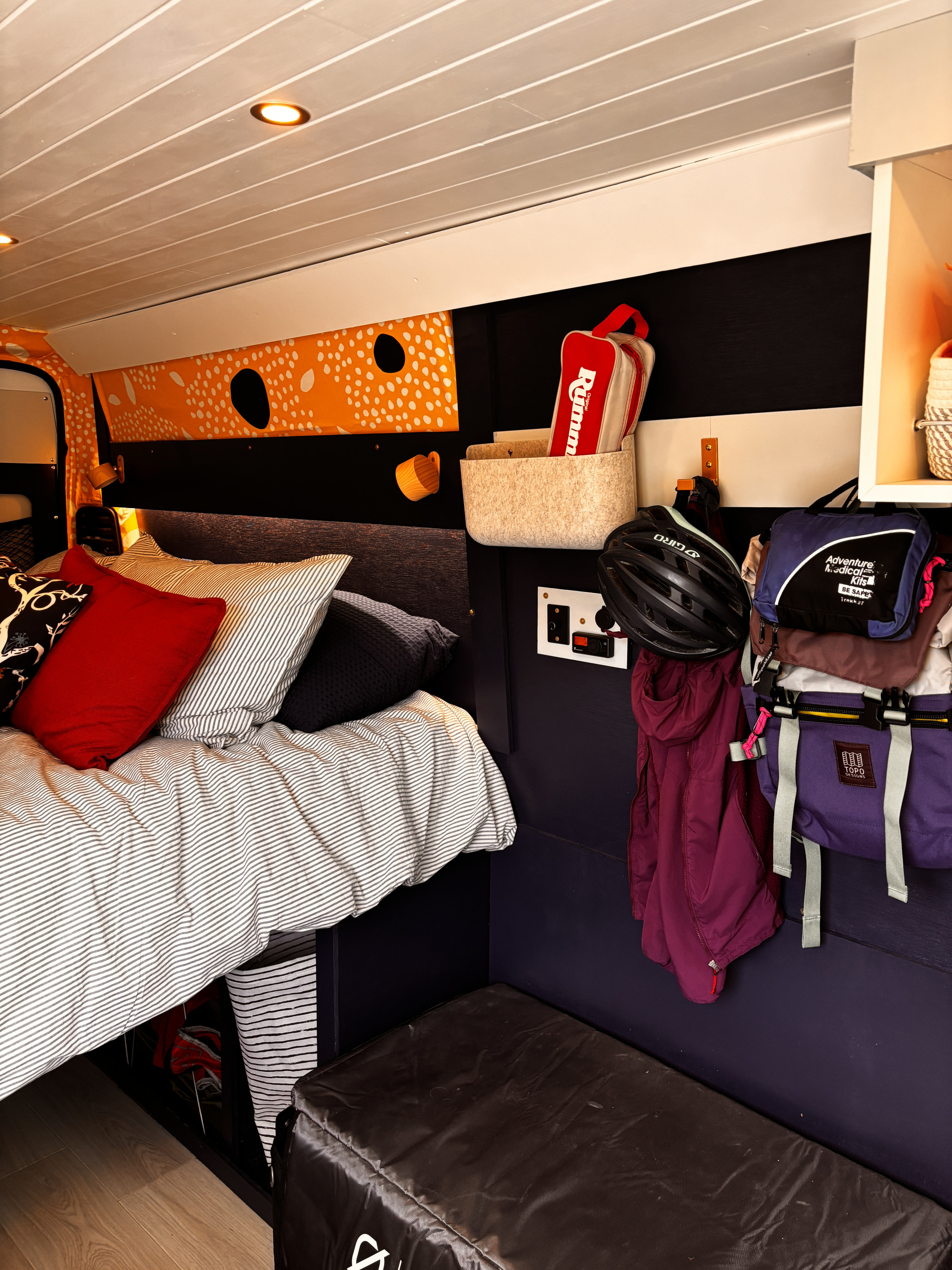 RV rental's inviting bedroom: comfy bed, vibrant decor, and efficient wall storage for a bike helmet & travel essentials.. RAM Promaster 2500 High Roof 159" WB 2023