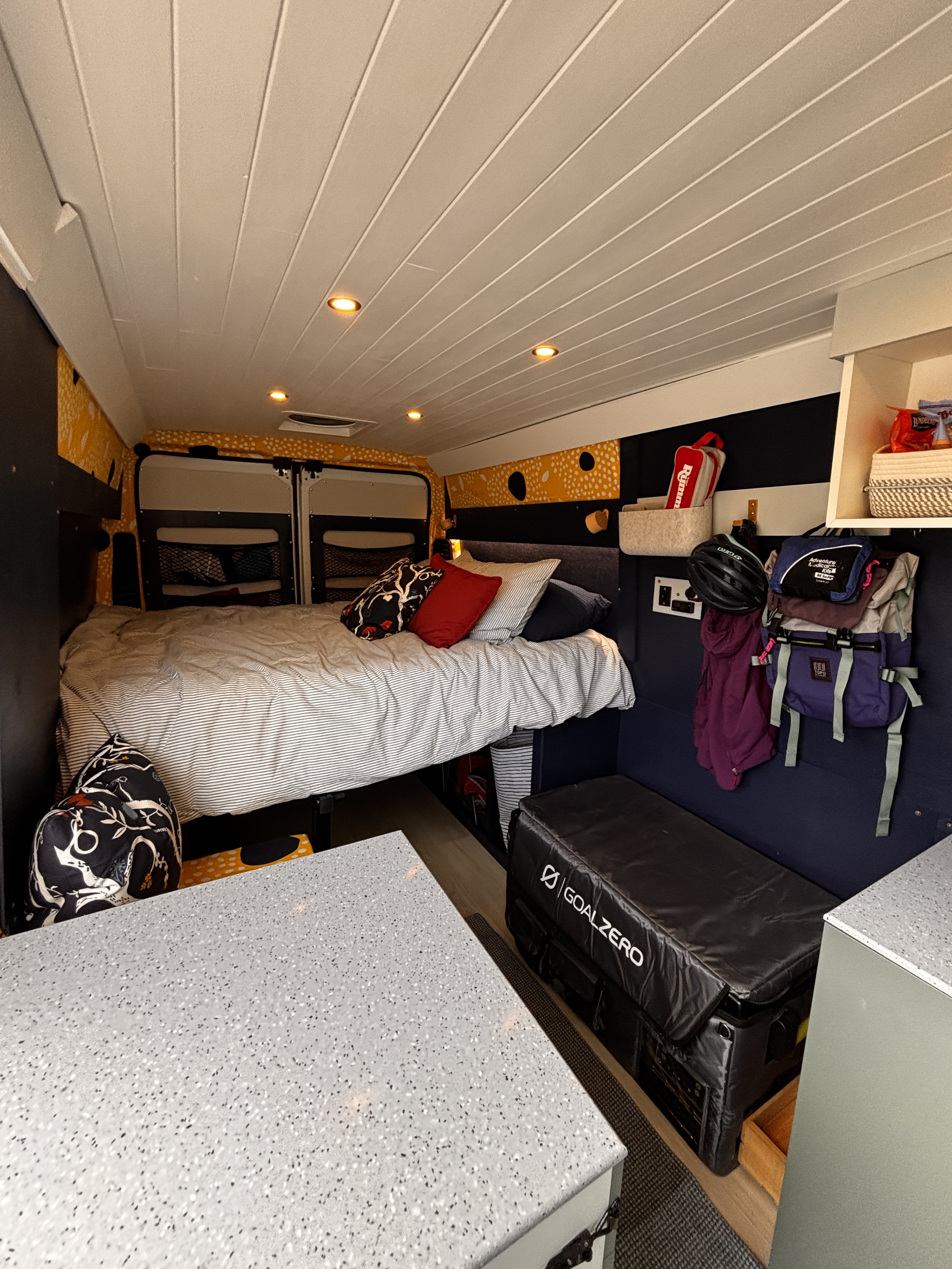 Cozy RV rental interior: A comfortable bed, ample storage including hanging gear, white slatted ceiling lights, and modern counter space.. RAM Promaster 2500 High Roof 159" WB 2023