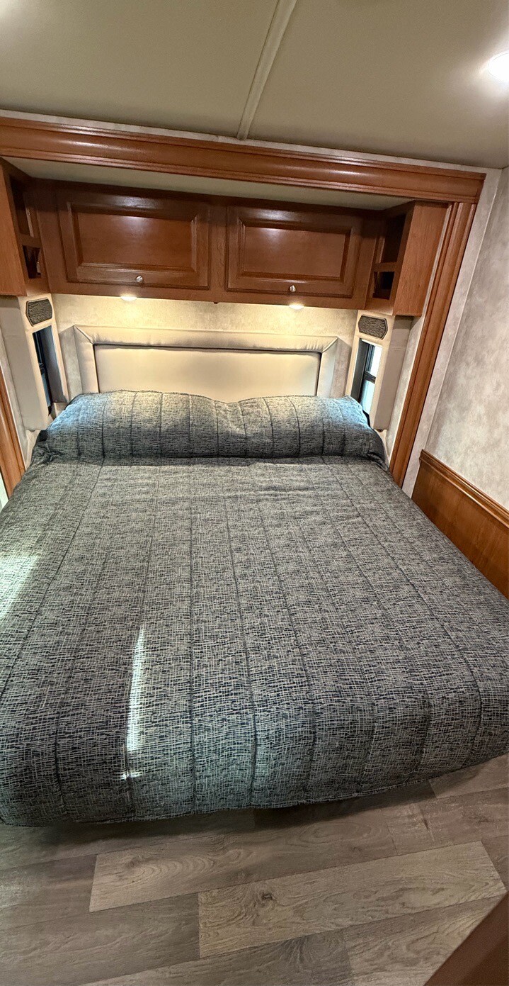 Comfortable RV rental bedroom features a large bed, upholstered headboard, and overhead wood cabinets.. Winnebago Adventurer 2020