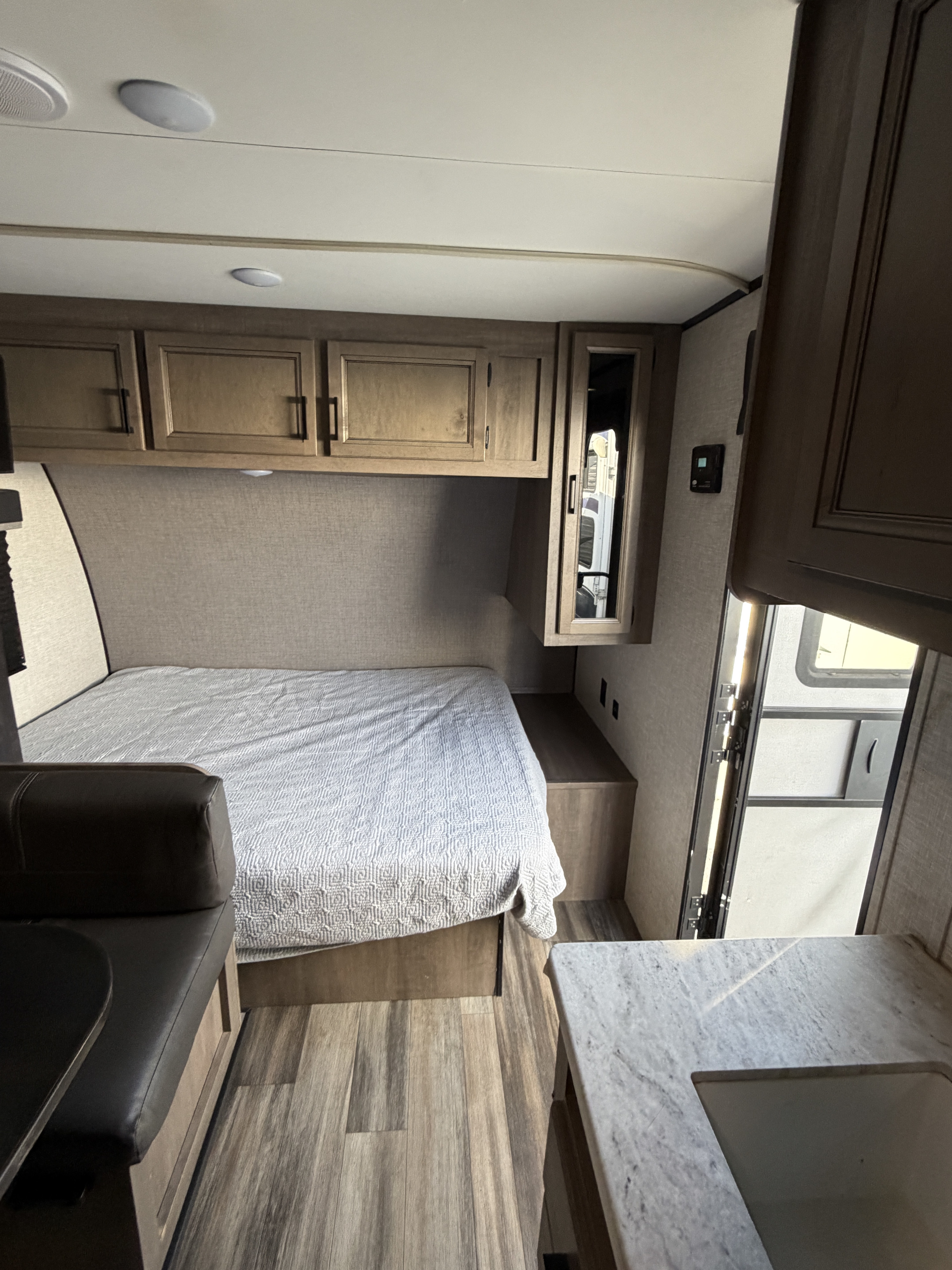 RV rental interior: A compact bedroom with overhead storage, a comfortable bed, and part of the kitchen countertop.. Starcraft Autumn Ridge 2023