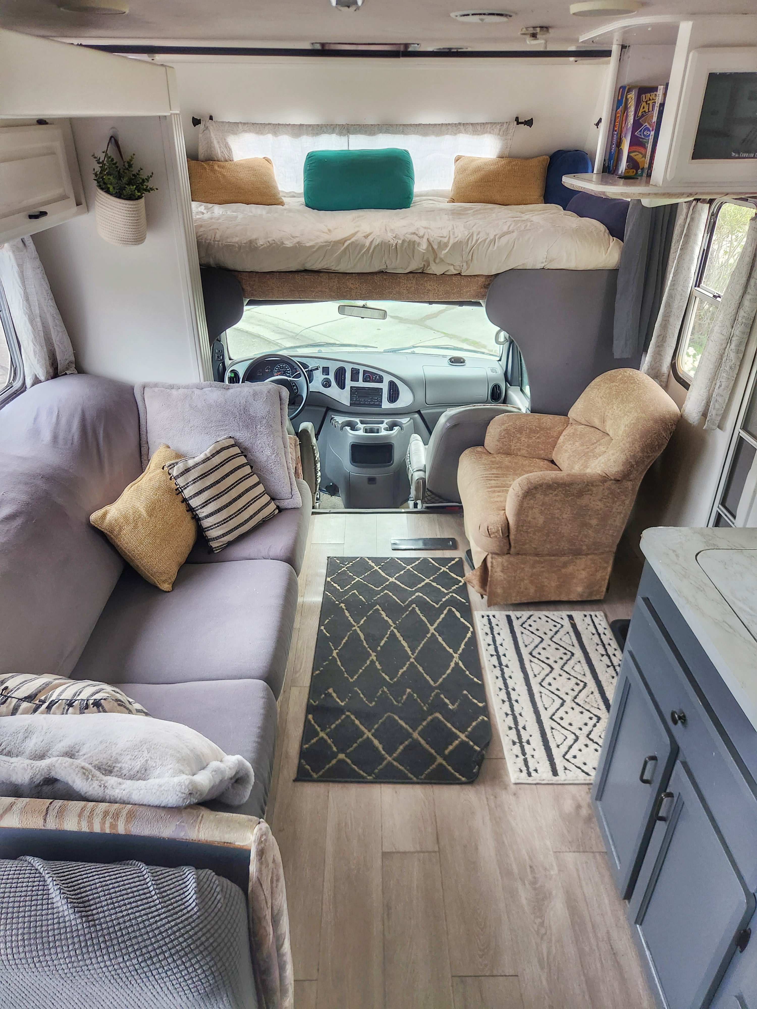 This RV rental showcases a cozy interior with a sofa, armchair, overhead bed, and kitchen.. Jayco Greyhawk 2002