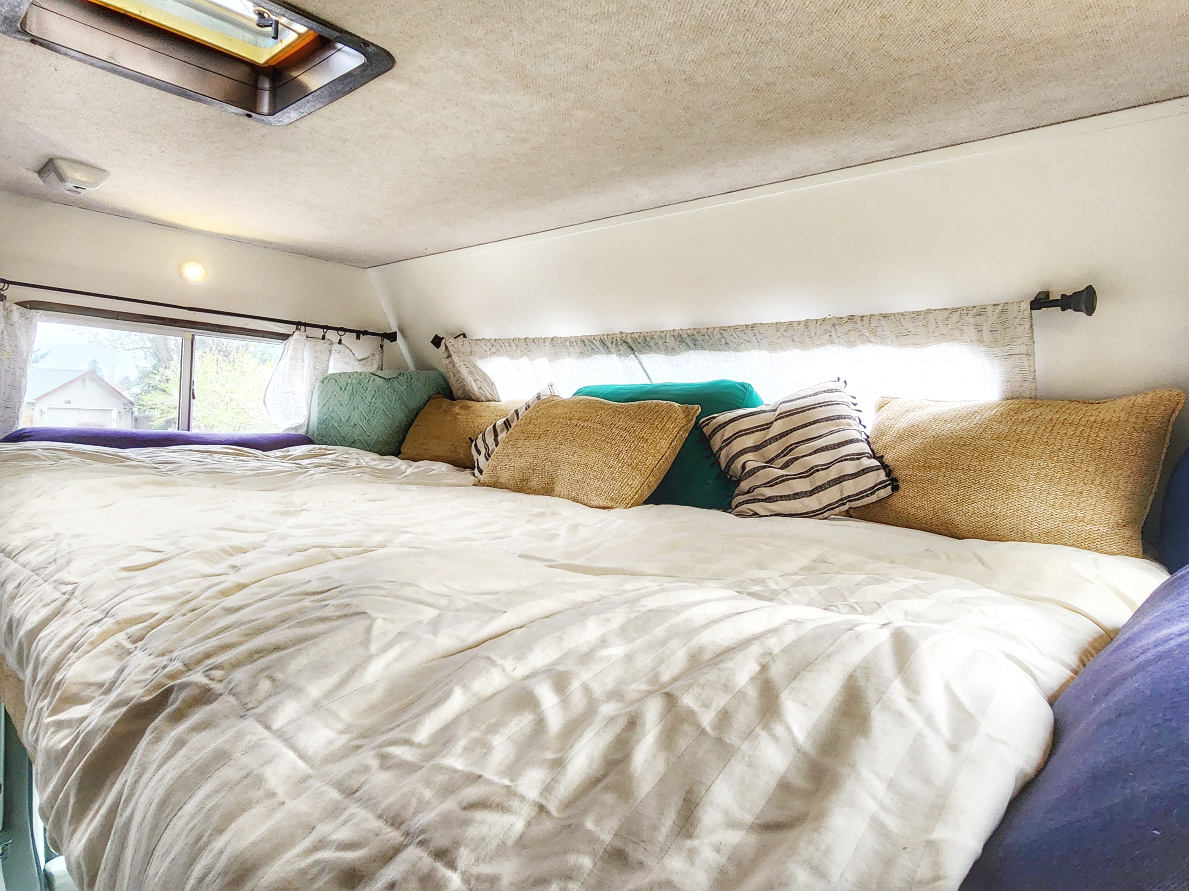Comfortable RV rental bed with fluffy pillows, a bright window view of trees, and an overhead skylight. A cozy sleeping area.. Jayco Greyhawk 2002