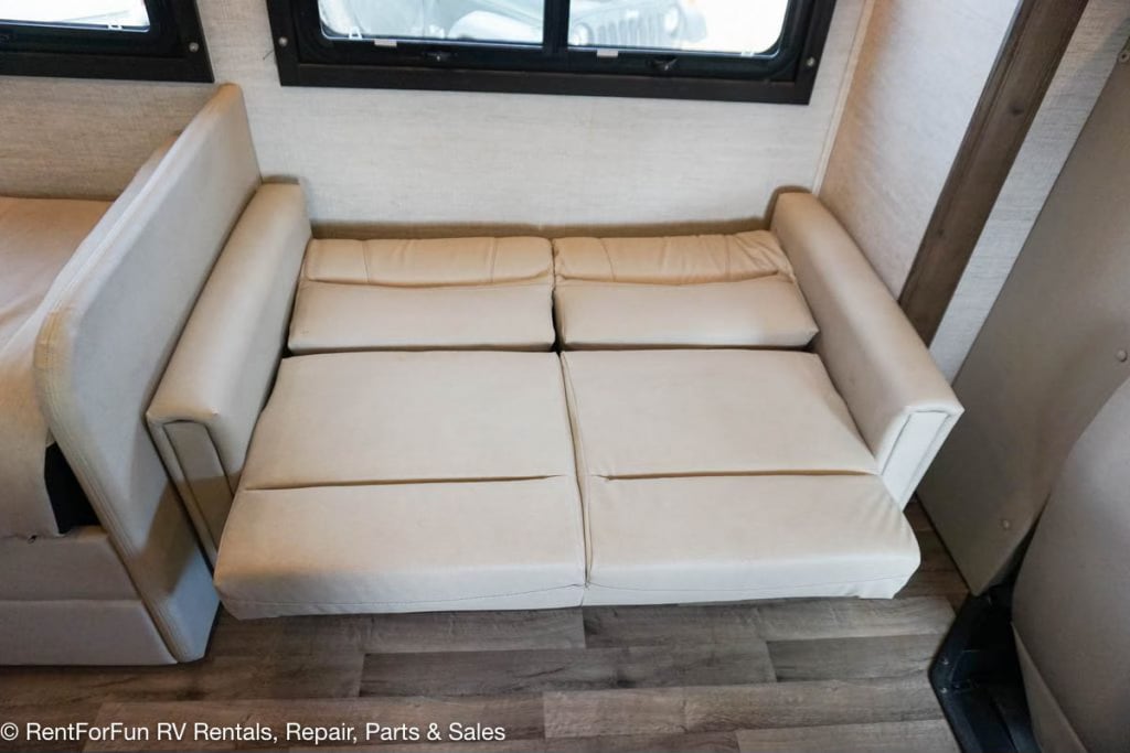 RV rental interior features a light-colored, extended sofa bed below windows, with wood laminate flooring.. Jayco Redhawk 2021