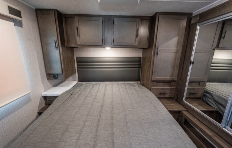RV rental: Bedroom with a queen bed, upholstered headboard, wooden cabinets, and a mirrored closet door.. Coachmen Leprechaun 2022