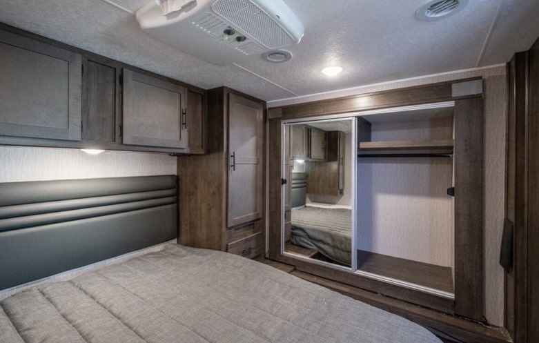 Modern RV rental bedroom with a bed, overhead storage cabinets, and a mirrored closet for compact, comfortable travel.. Coachmen Leprechaun 2022