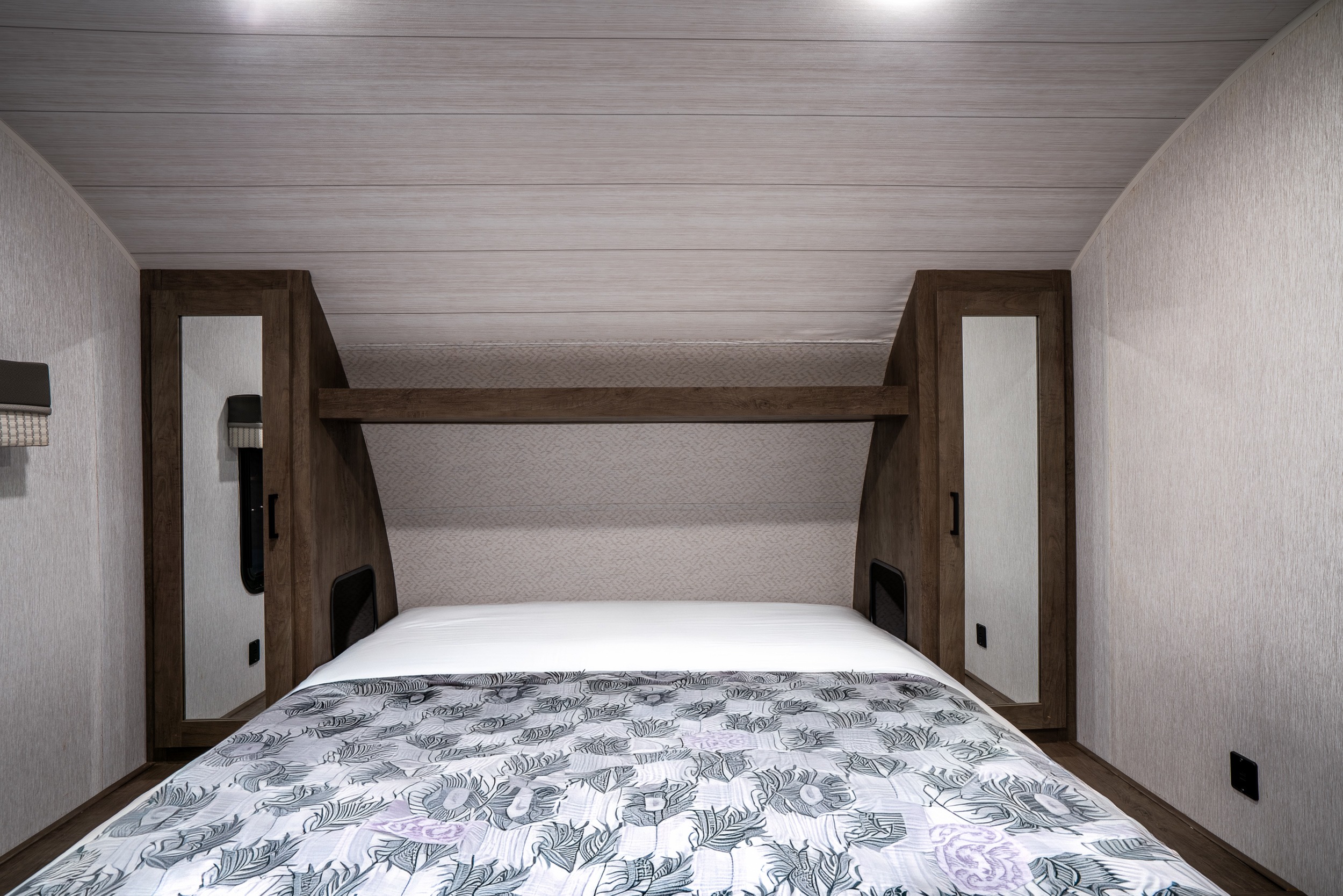 Cozy RV rental bedroom with a patterned bed, mirrored wardrobes, and wooden overhead storage. Light walls and ceiling.. Forest River Salem Cruise Lite 2022
