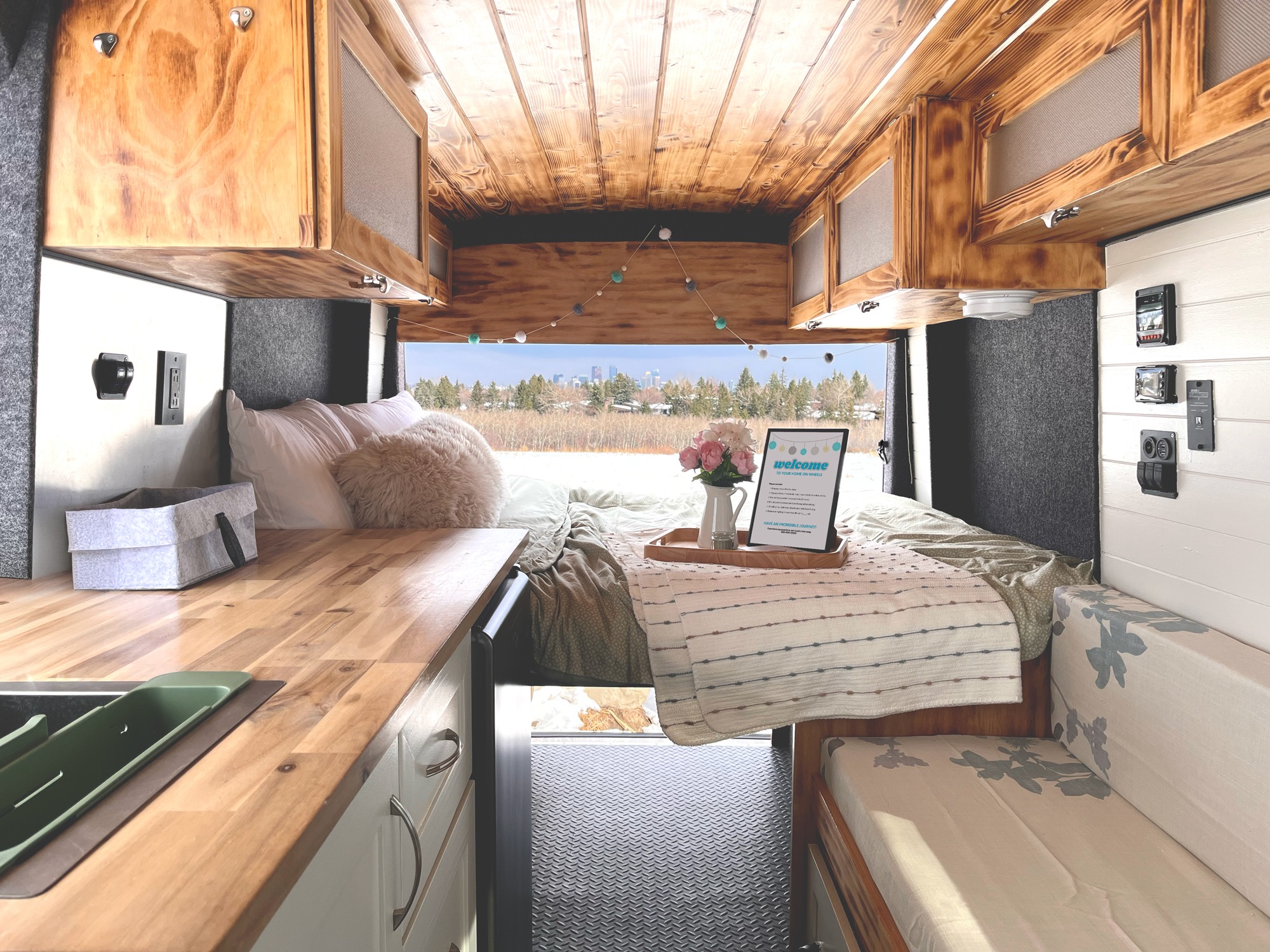 Cozy, modern **RV rental** interior with a bed, kitchen counter, and scenic window view, ideal for a comfortable van life experience.. Ford Transit T-250 2019