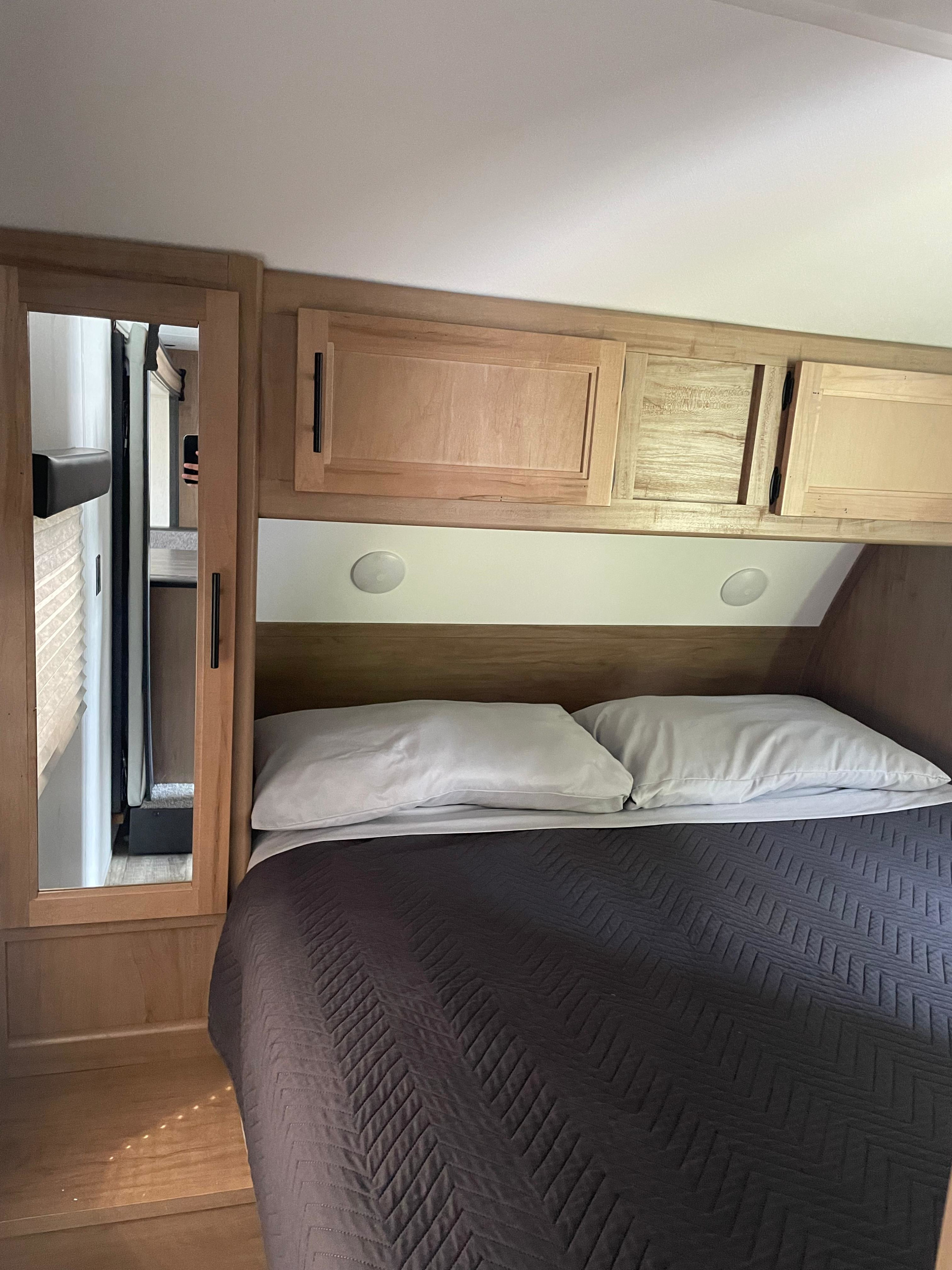 RV rental bedroom: a cozy retreat with a bed, white pillows, dark comforter, wooden cabinets, and a mirrored closet.. Forest River Cherokee Grey Wolf 2023