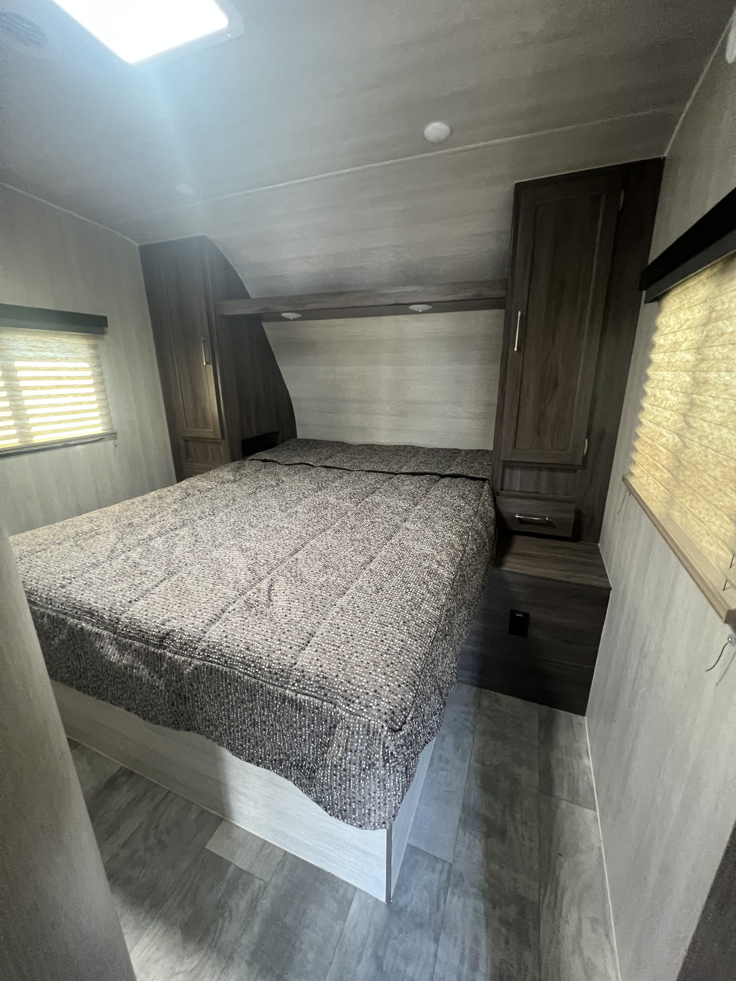 RV rental bedroom with patterned bed, dark wood cabinets, windows, light plank flooring, and overhead lighting.. Genesis Supreme Rv Genesis Supreme 2022