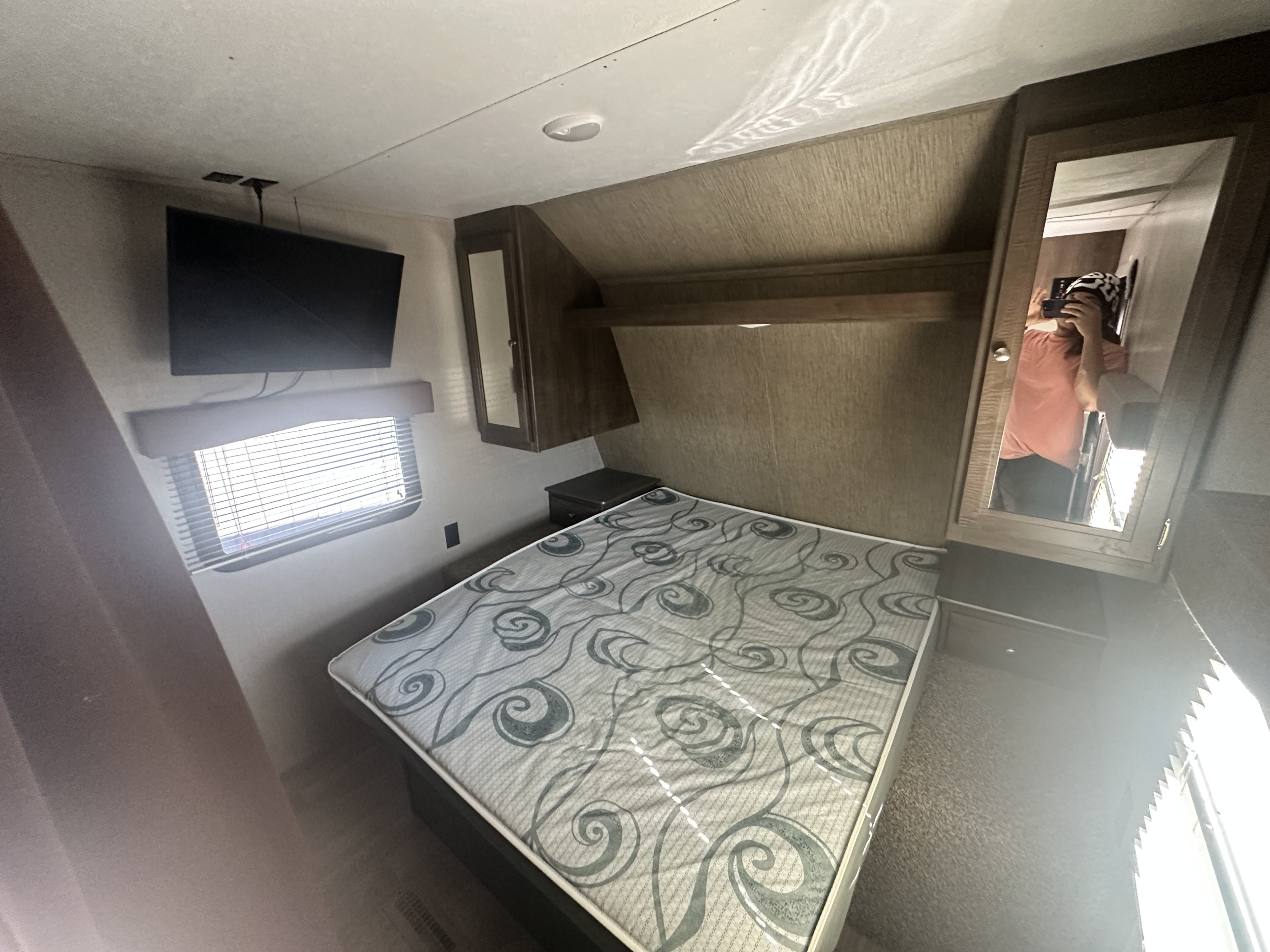 Cozy rv rental bedroom interior with a patterned mattress, wall-mounted TV, window with blinds, and mirrored cabinet for travel.. Keystone RV Coleman 2019