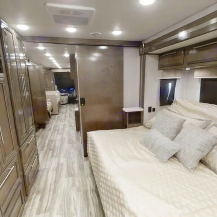 Spacious RV rental interior featuring a cozy bedroom, light wood flooring, and ample built-in cabinets in the hallway.. Forest River Georgetown 2022