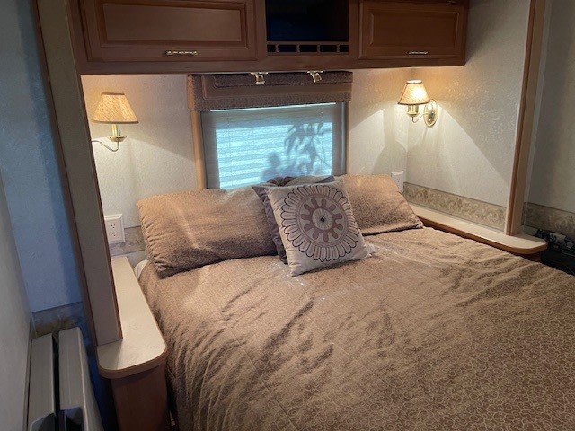 An inviting RV rental bedroom featuring a full-size bed, overhead storage, and warm wall sconces.. Jamboree Sport 2011