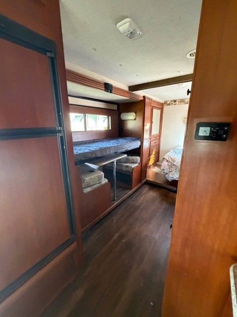 Interior of an RV rental showing a bunk bed, a compact dinette with table, dark wood-style flooring, and a control panel.. Jamboree Sport 2011