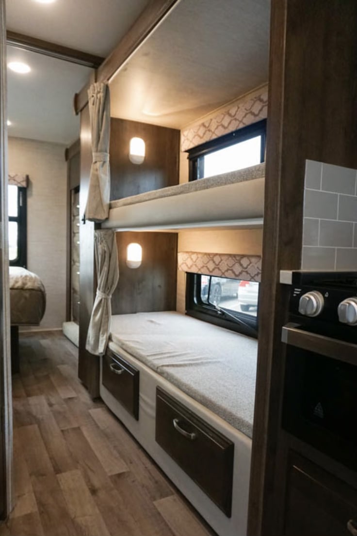 Experience a cozy RV rental: bunk beds with individual lights and windows, and a glimpse of the integrated kitchen.. Jayco Redhawk 2021