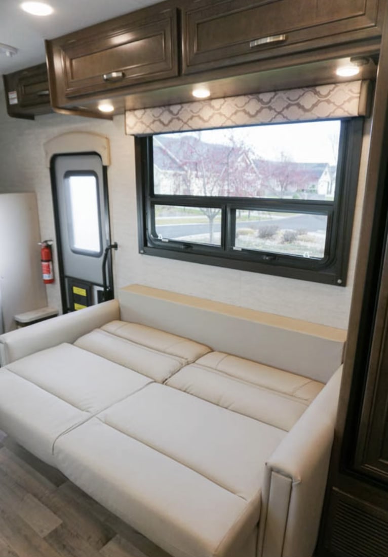 Comfortable RV rental interior featuring a convertible sofa, a bright window view, and overhead storage cabinets.. Jayco Redhawk 2021