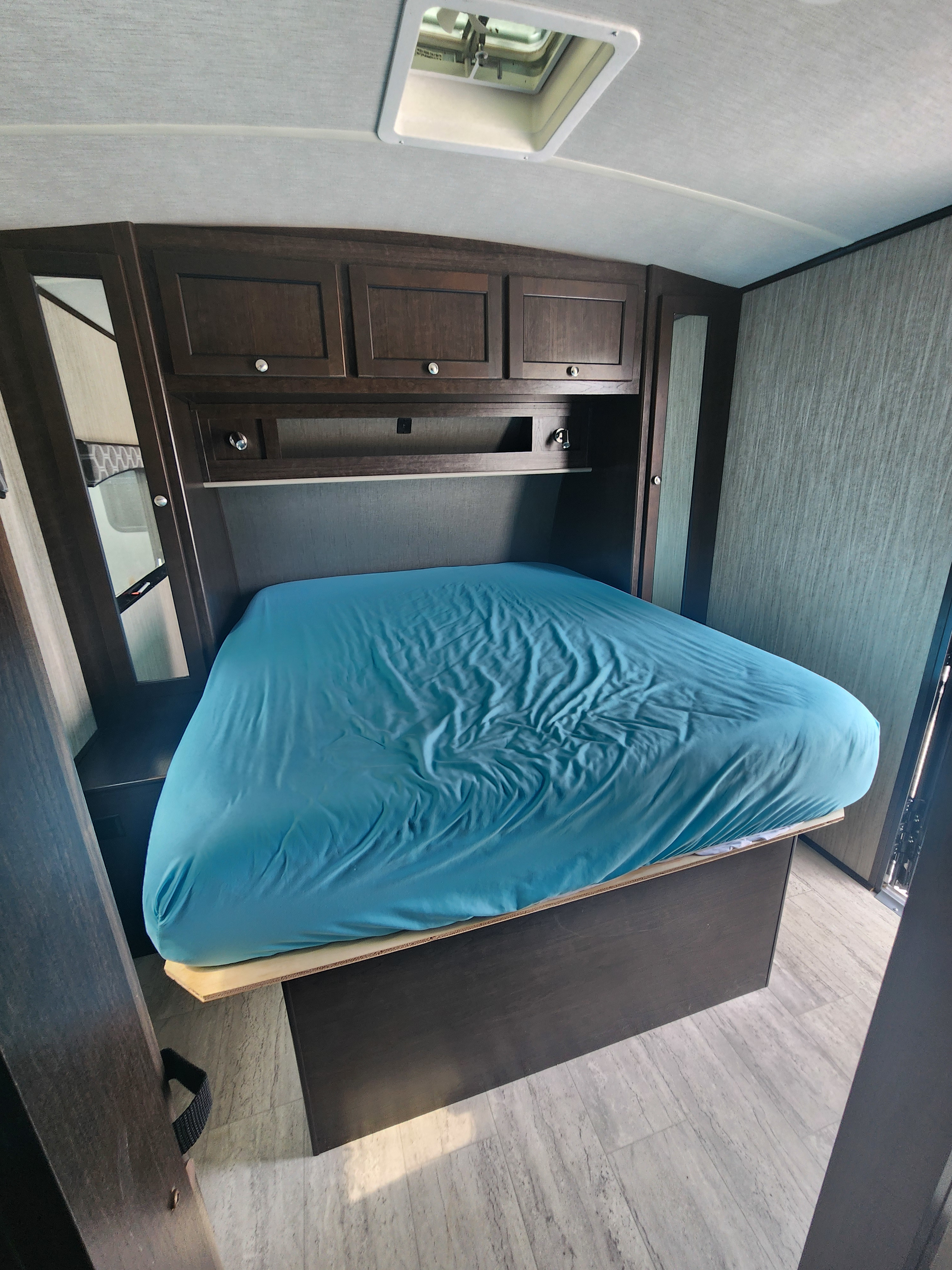 Clean RV rental bedroom. Features a blue-sheeted bed, dark wooden cabinets, and a ceiling vent for comfortable travels.. Cruiser RV Shadow Cruiser 2019