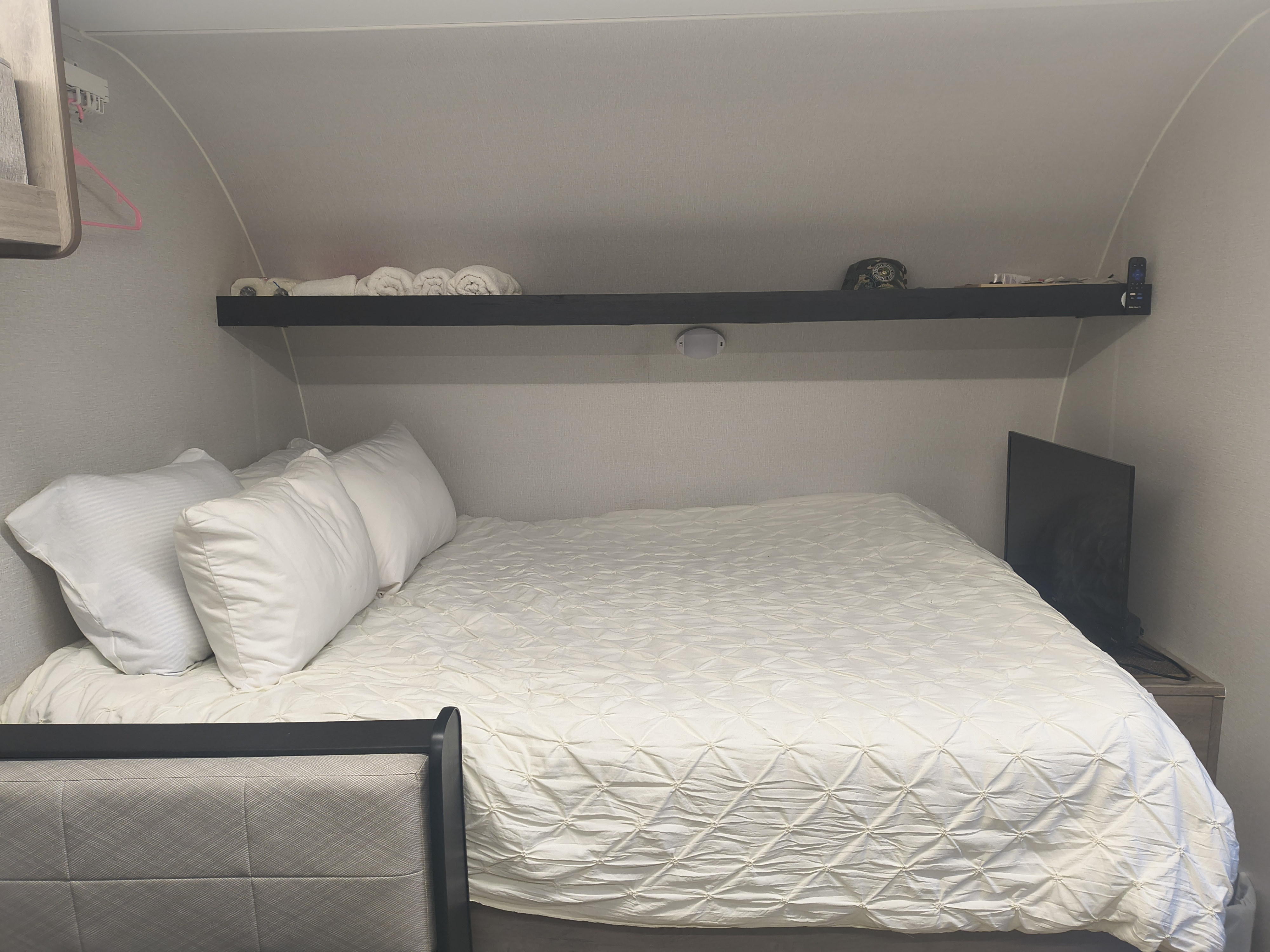 This RV rental bedroom features a comfortable bed with white pillows & comforter, an overhead shelf, and a TV.. Cruiser RV Embrace 2025