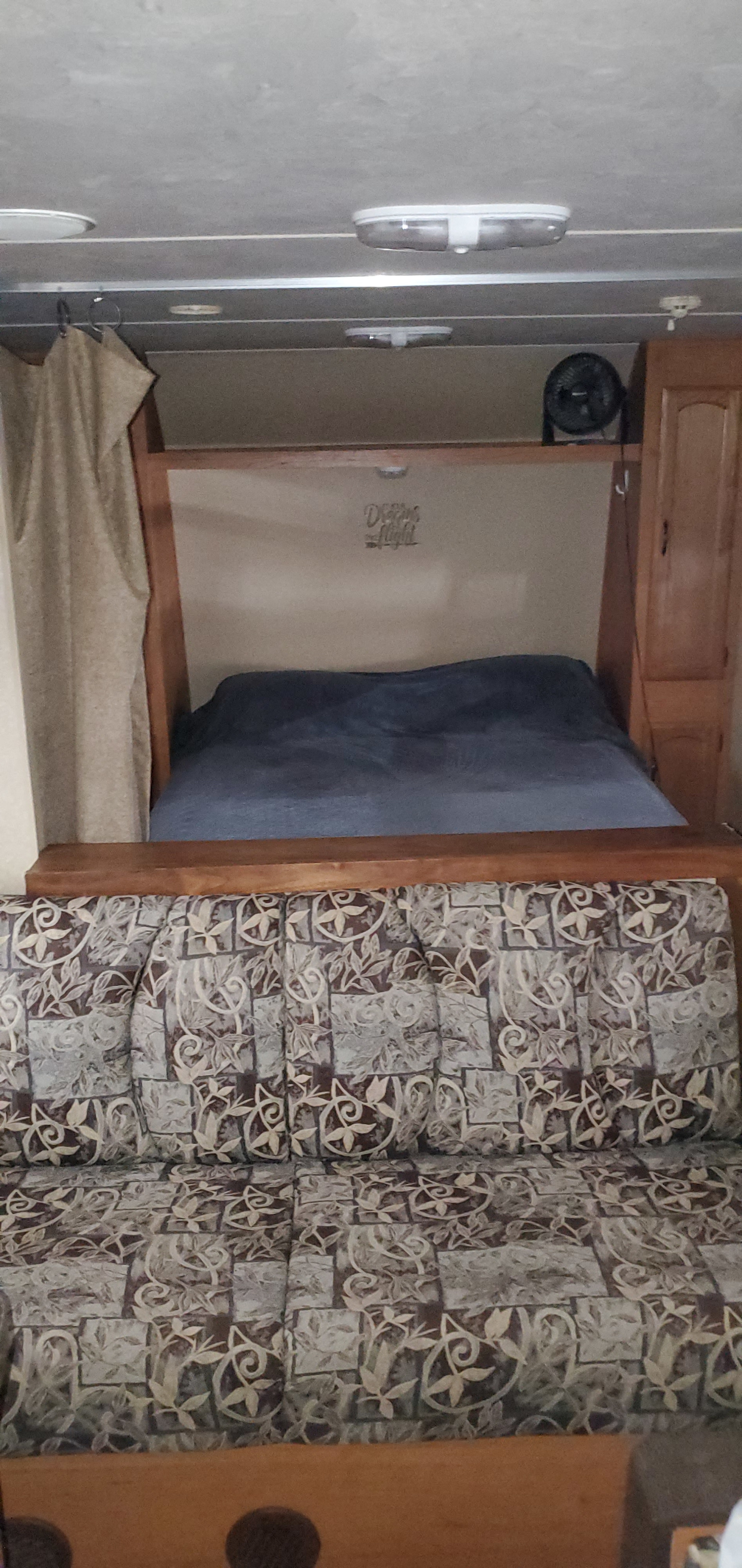 Inside this RV rental: a comfortable bed with a dark blue blanket, a patterned sofa, and overhead lights.. Forest River Wildwood X-Lite 2011