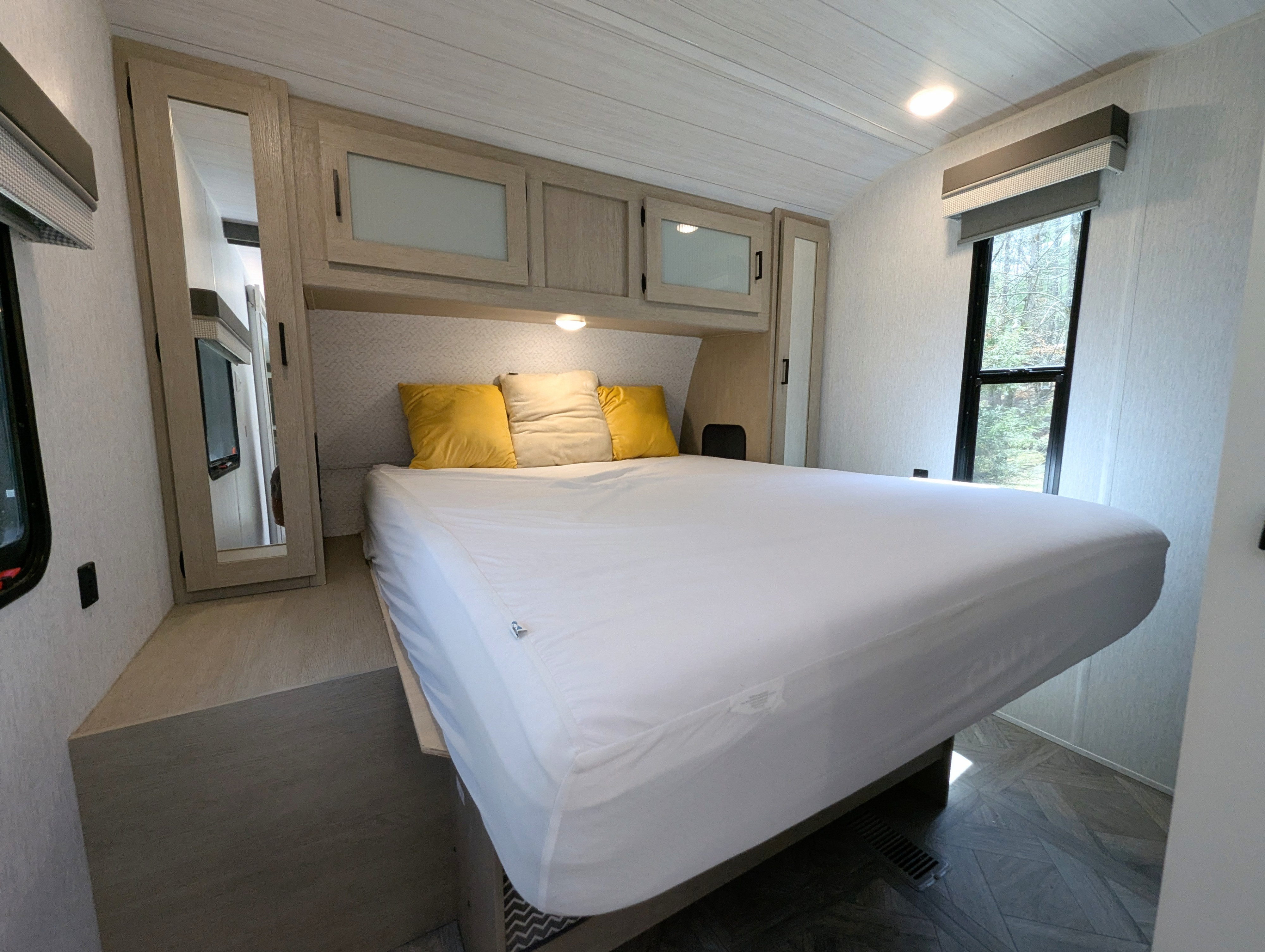 Comfortable RV rental bedroom featuring a queen bed with overhead storage, mirrored closets, and a window with blinds.. Forest River Wildwood 2023