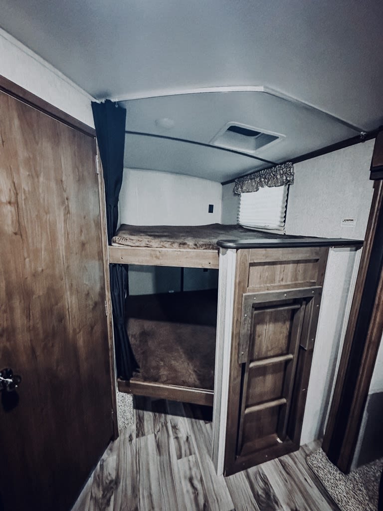 RV rental interior shows bunk beds with dark bedding, privacy curtains, and a foldable ladder on wood-look flooring. Great for families.. Keystone RV Cougar 2019