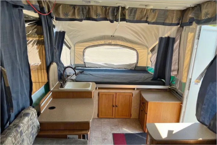 Inside a pop-up RV rental, featuring a comfortable bed, compact kitchen with sink, and seating area, perfect for camping.. Forest River Palomino Y-Series 2010