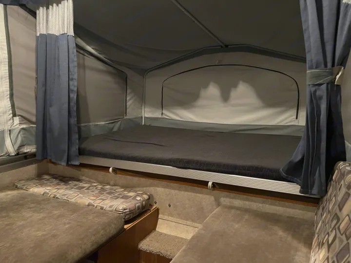 Cozy sleeping area in an RV rental pop-up camper with a dark mattress, canvas walls, and patterned bench seating.. Forest River Palomino Y-Series 2010
