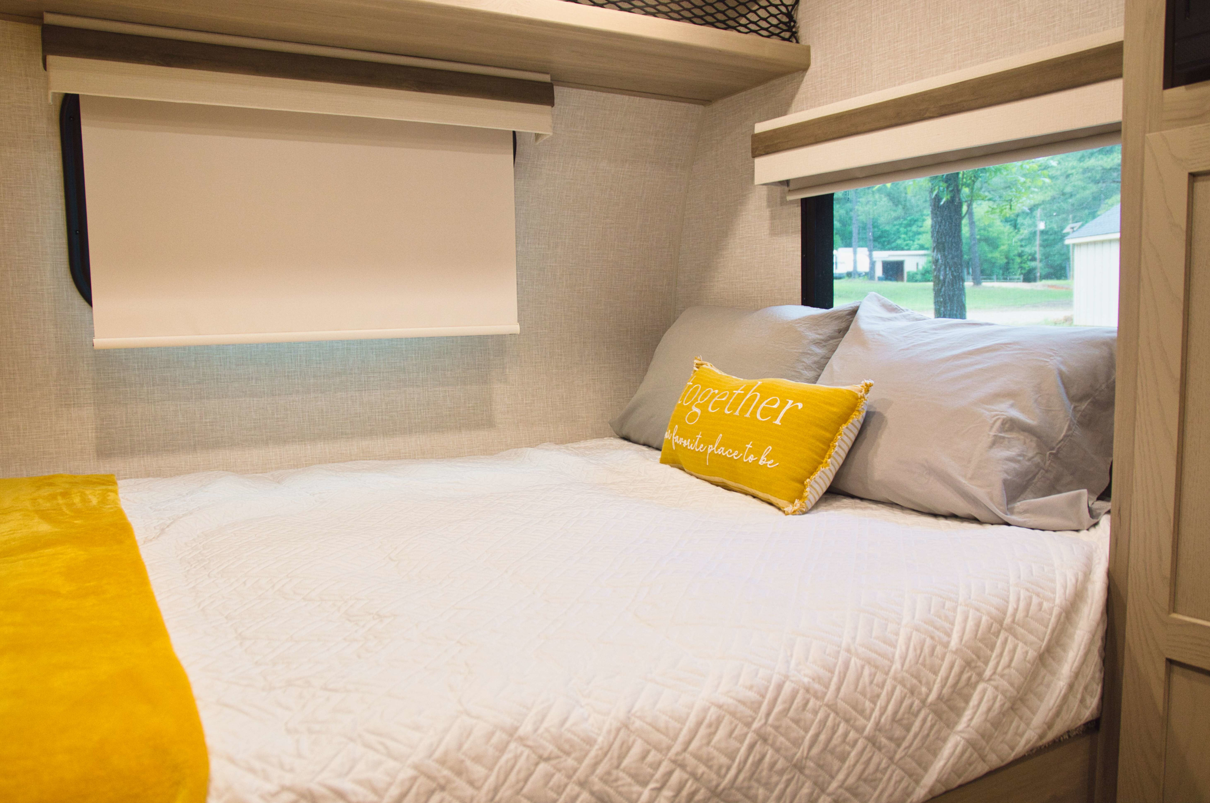 Bright & cozy RV rental bedroom. Features a white quilted bed with yellow accents & decorative pillows by a window.. Forest River Rockwood Geo Pro 2024