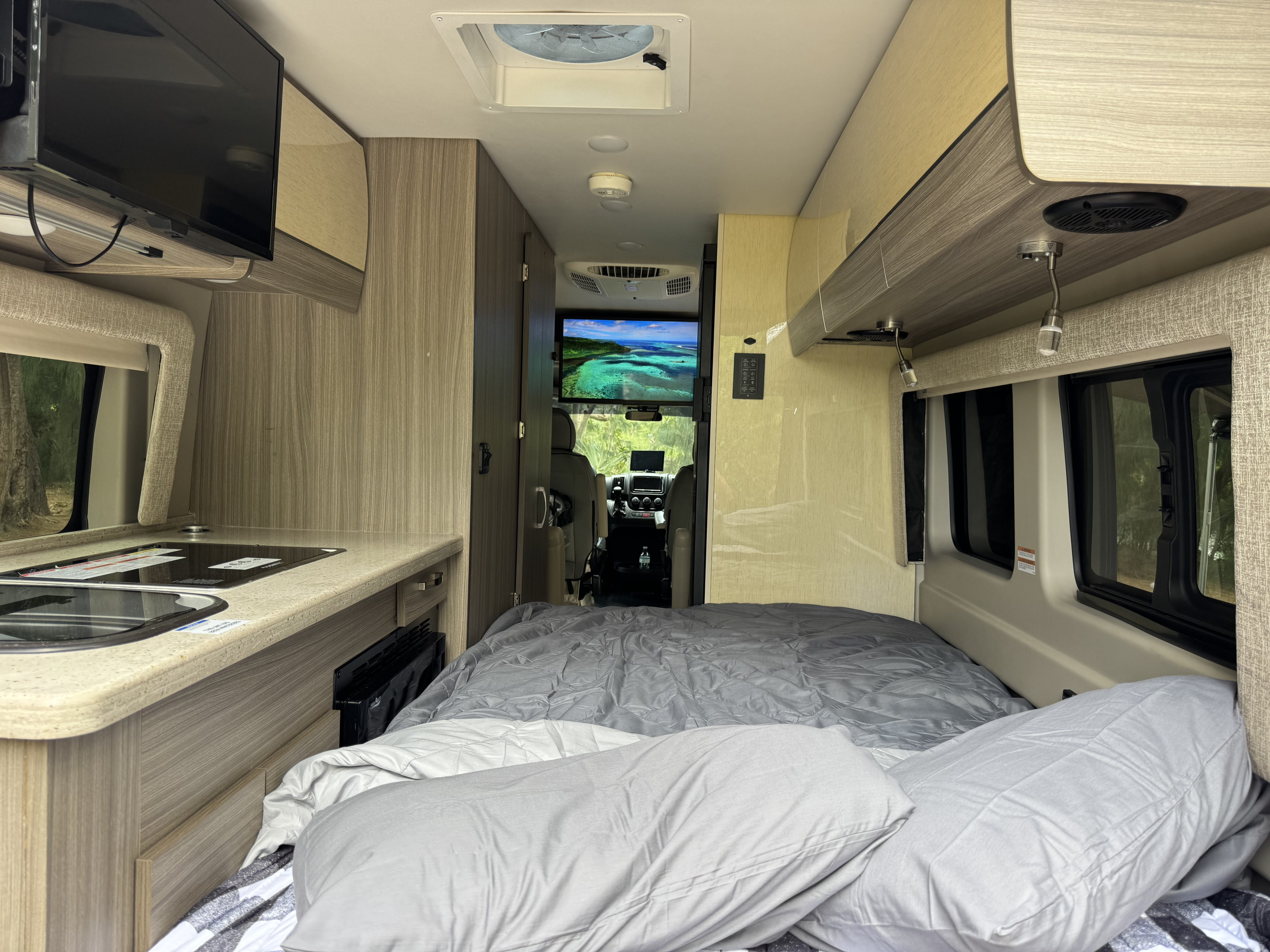 Inside a modern rv rental: comfortable bed, kitchen with sink & stovetop, TV showing a beautiful ocean scene, ready for adventure.. Entegra Coach Ethos 20a 2022
