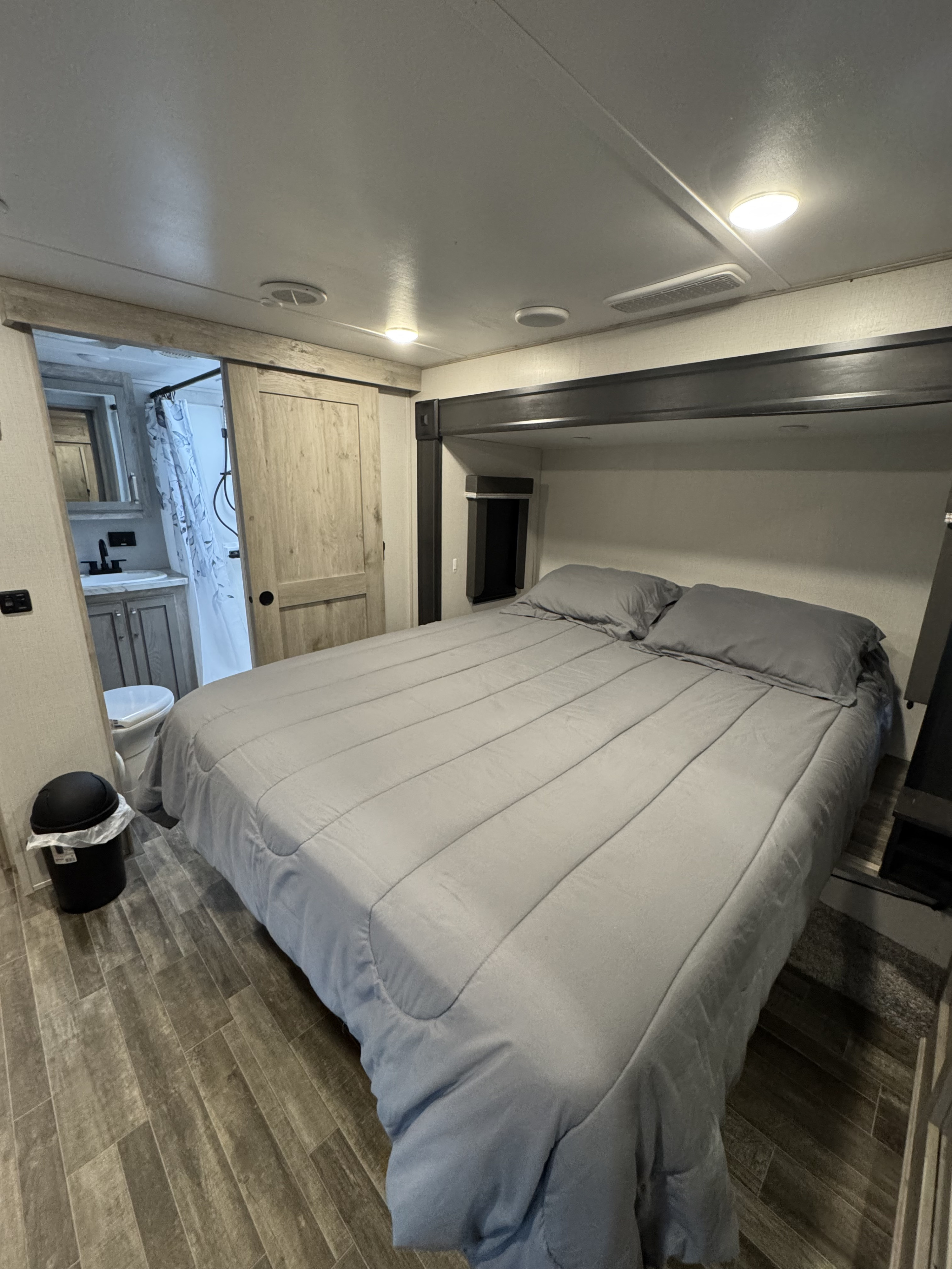 Spacious RV rental bedroom featuring a comfy grey bed, wood-look floor, and an en-suite bathroom with a sliding barn door.. Keystone RV Avalanche 2021
