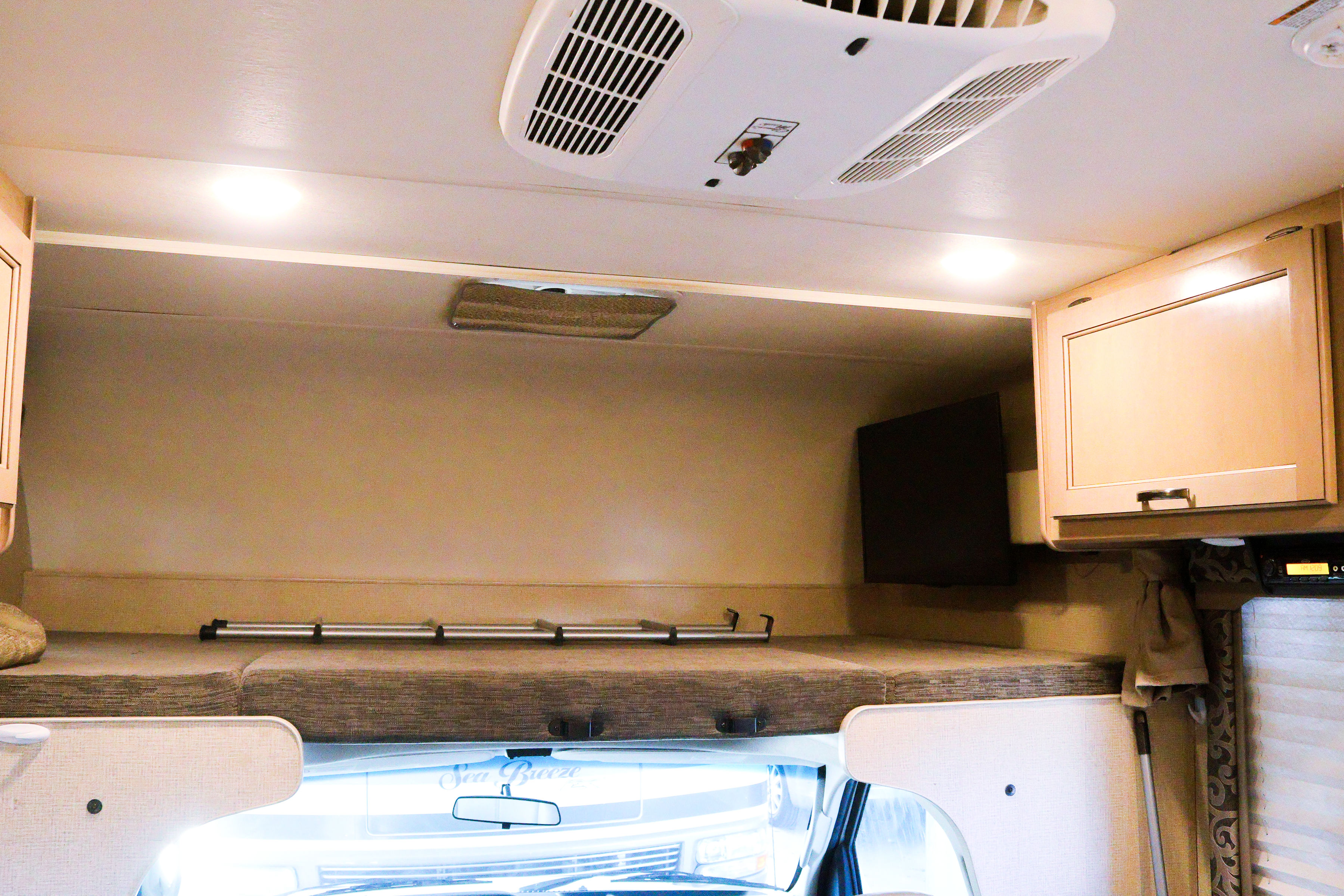 RV rental interior: front overhead bunk bed with a ladder, wall-mounted TV, air conditioner, & storage cabinet.. Thor Four Winds 2019