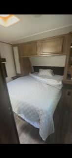 RV rental bedroom with a cozy bed, wooden overhead cabinets, and a skylight. Comfortable and compact interior.. Jayco Jay Feather 2019