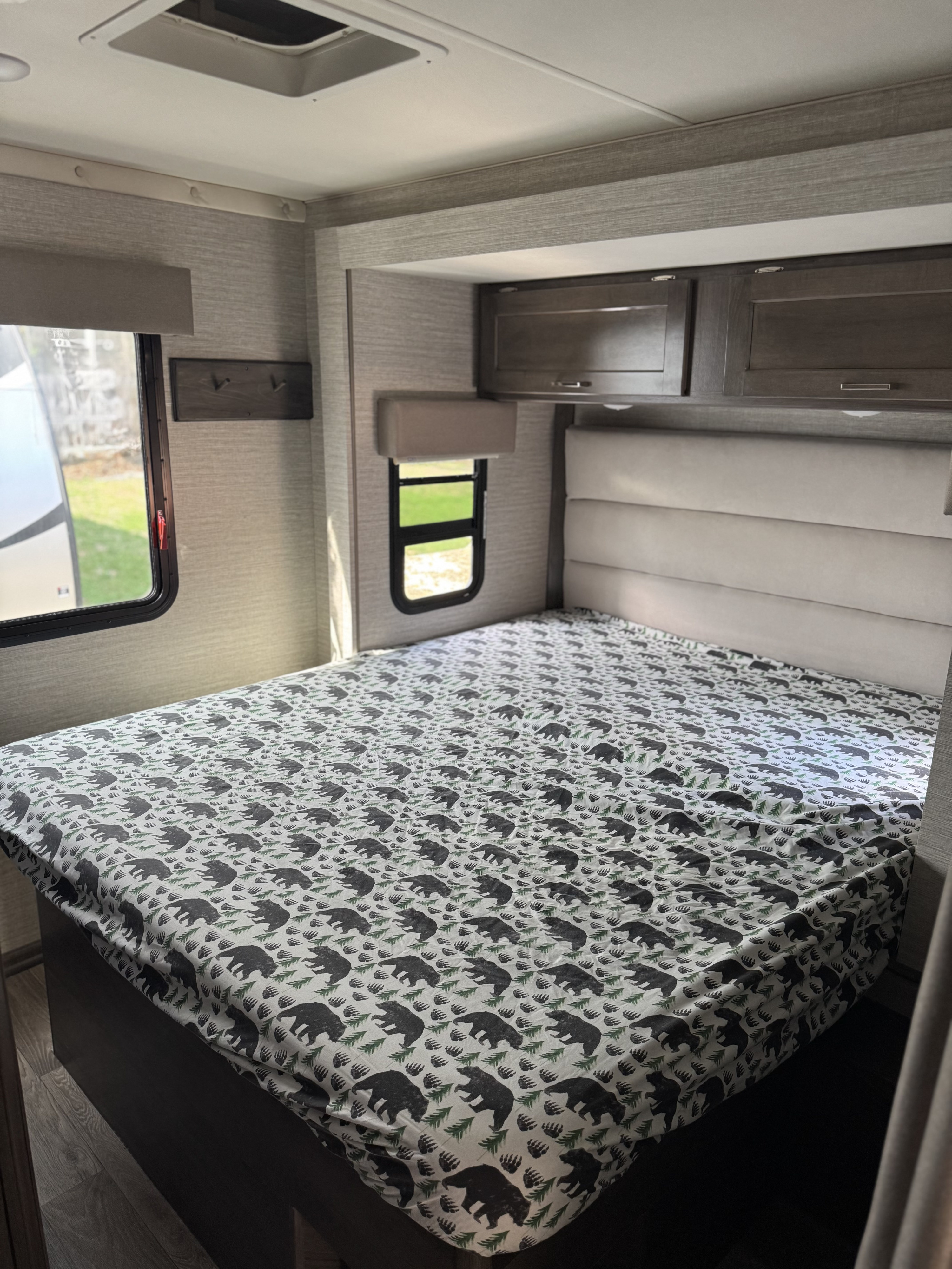 An RV rental bedroom featuring a bed with a charming bear-patterned cover, windows, and overhead cabinets.. Winnebago Minnie Winnie 2020