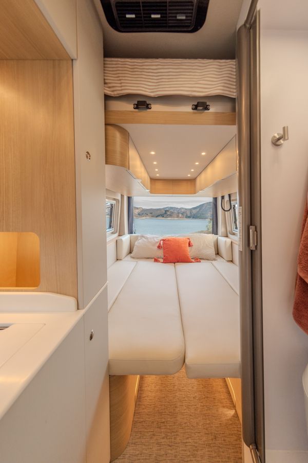 Experience comfort in this RV rental's spacious interior, featuring a cozy bed and stunning panoramic views of a lake and mountains.. Noovo Noovo Class B 2024